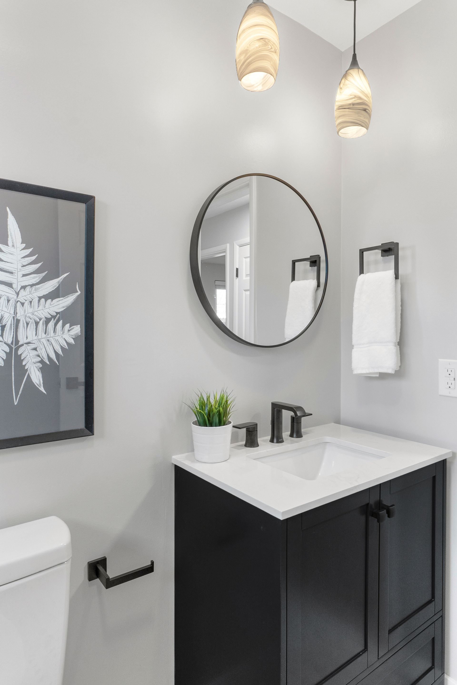 Bathroom with black vanity, round mirror, white sink, and fern artwork on a gray wall.