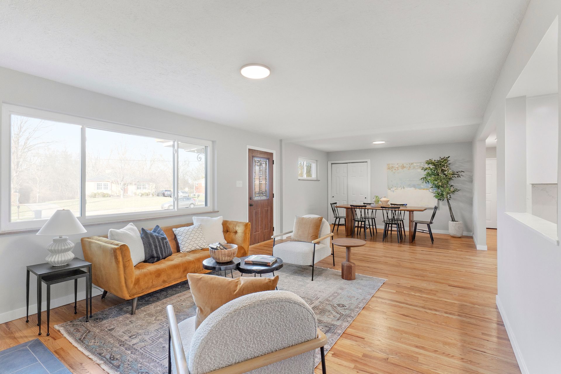 Bright living room with mustard sofa, rug, wood floors, and dining area.