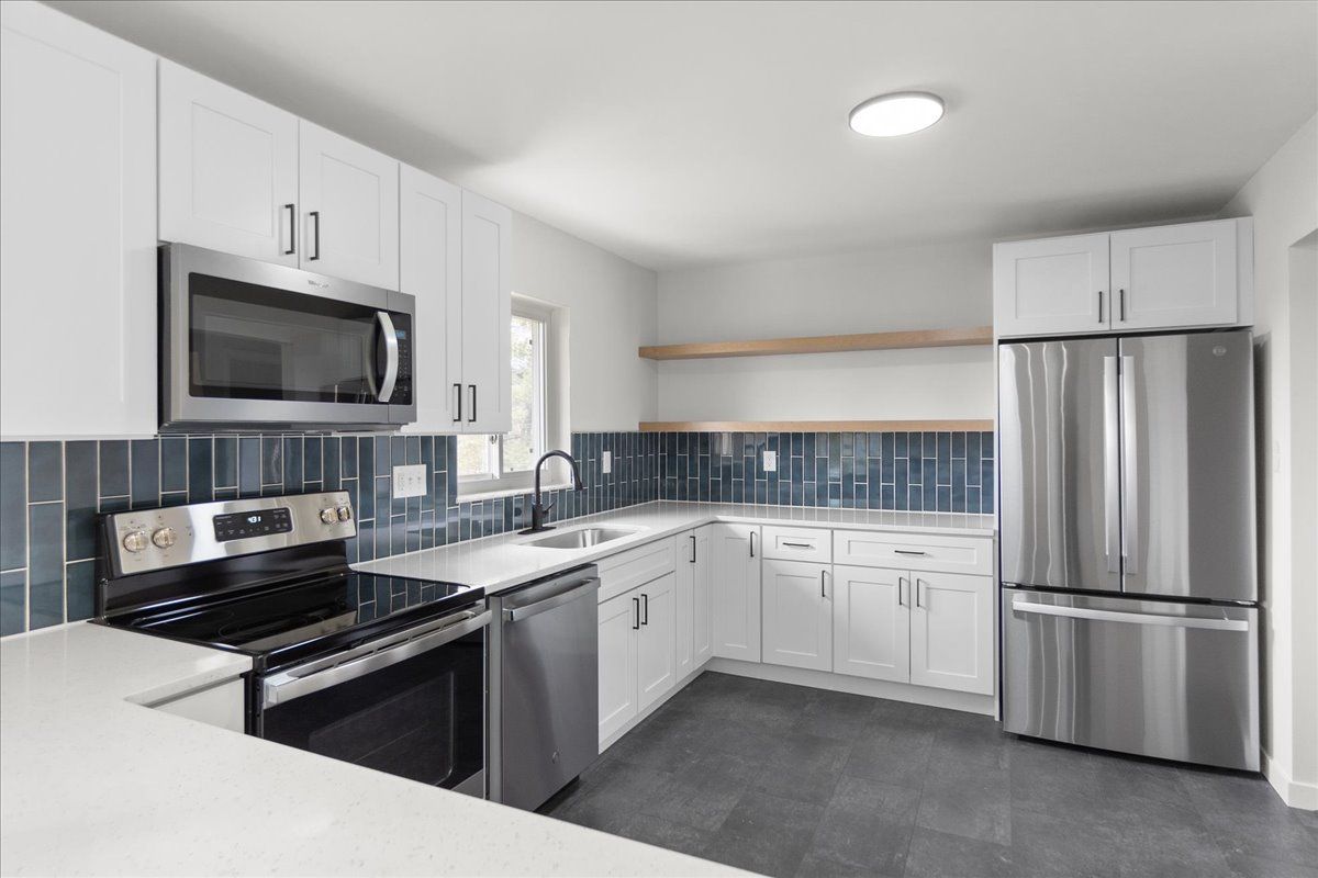 White kitchen with stainless steel appliances, blue tiled backsplash, and light gray floors.