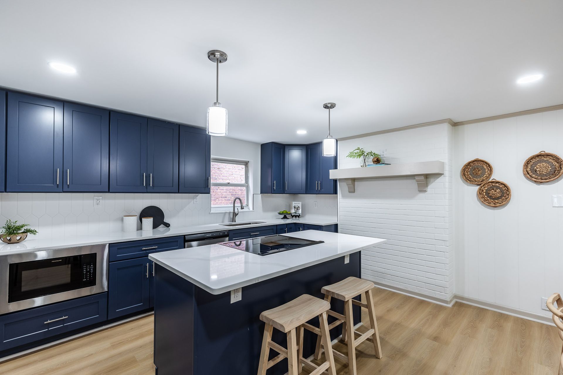 Modern kitchen with blue cabinets, white countertops, and wood flooring; island with stools.