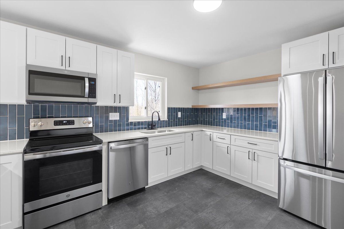 Modern kitchen with white cabinets, stainless steel appliances, blue tile backsplash, and dark floor.