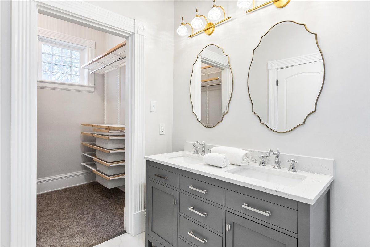 Bathroom with gray vanity, two oval mirrors, and a walk-in closet.
