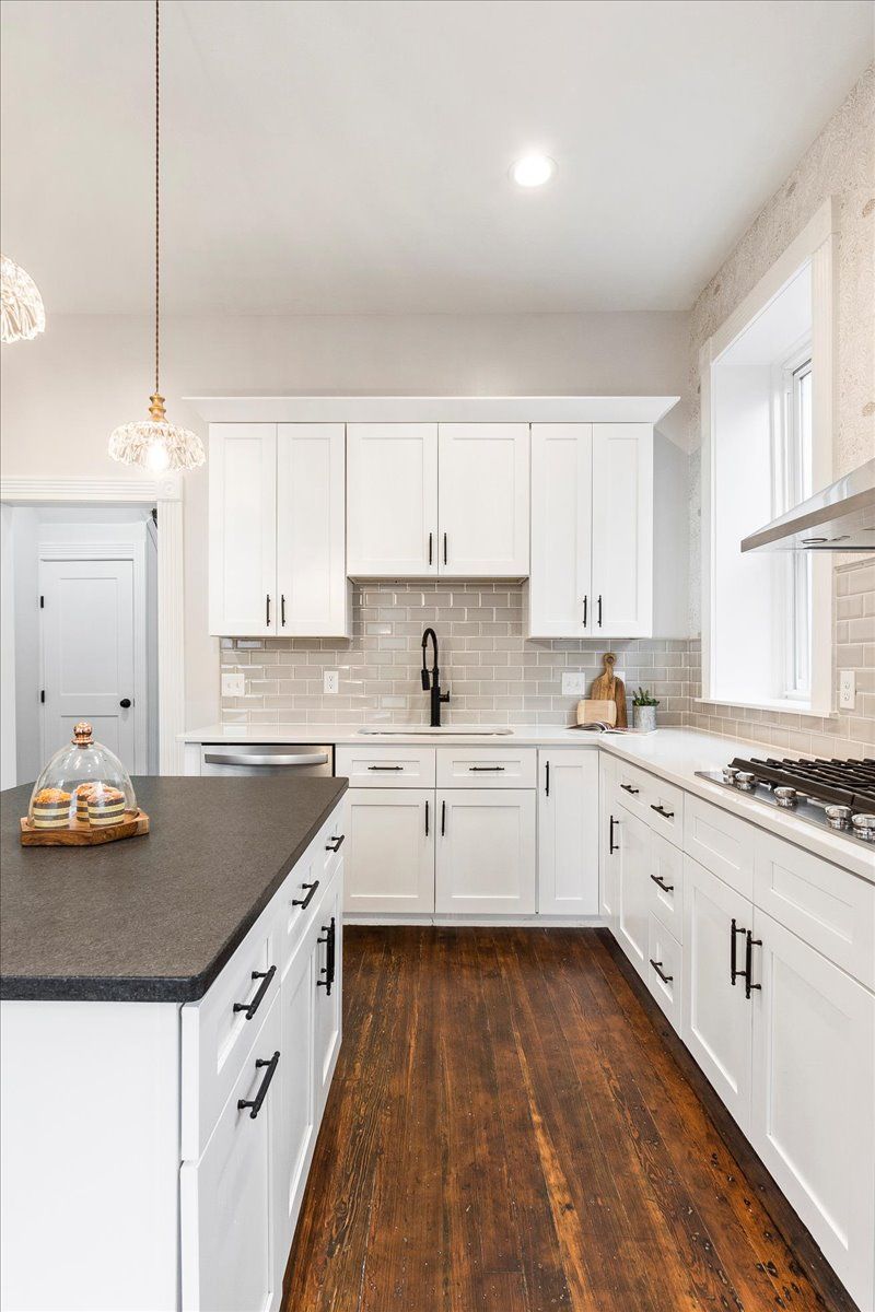 White kitchen with dark wood floor, white cabinets, black countertops, island, and stainless steel appliances.