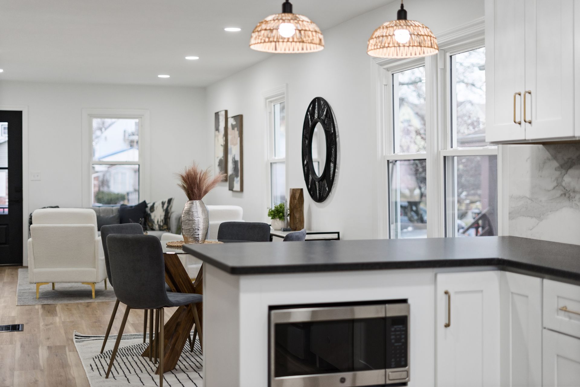 Modern kitchen and dining area with white cabinets, dark countertops, and woven pendant lights.