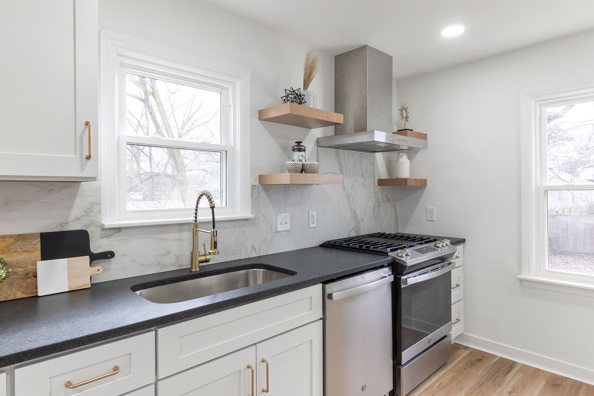 Modern kitchen with white cabinets, black countertop, stainless steel appliances, and floating shelves.