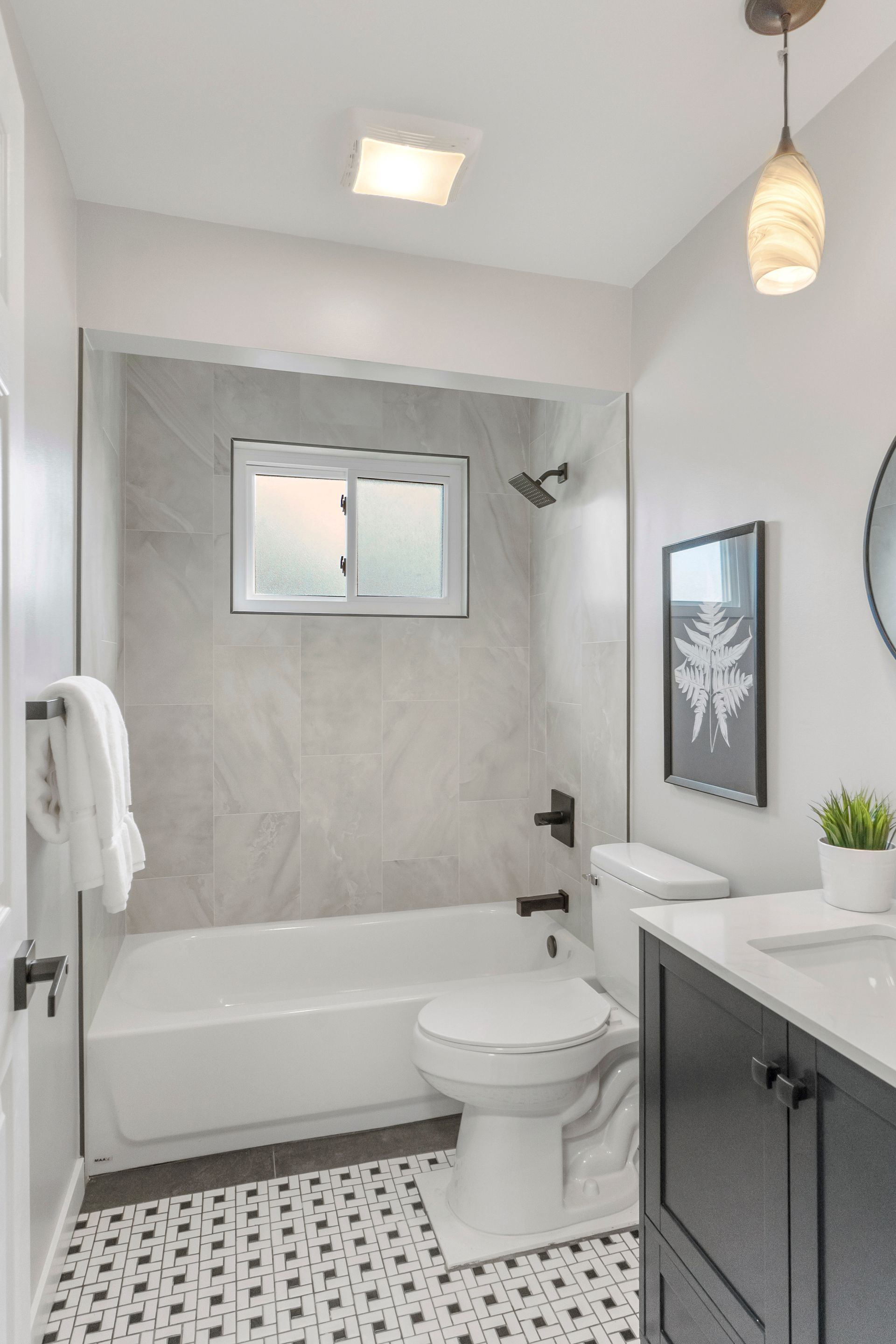 Bathroom with white tub, toilet, and vanity. Gray walls and patterned floor.