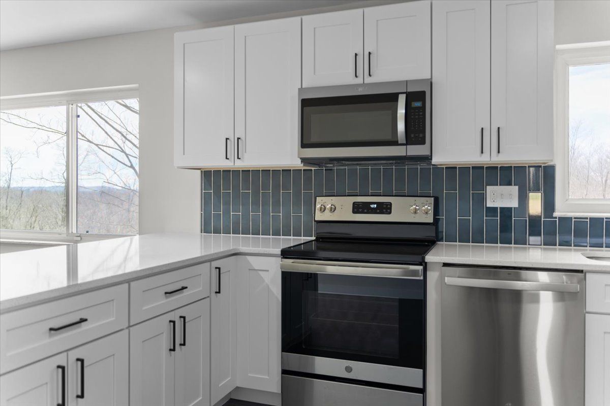 White kitchen with blue tiled backsplash, stainless steel appliances, and quartz countertops.