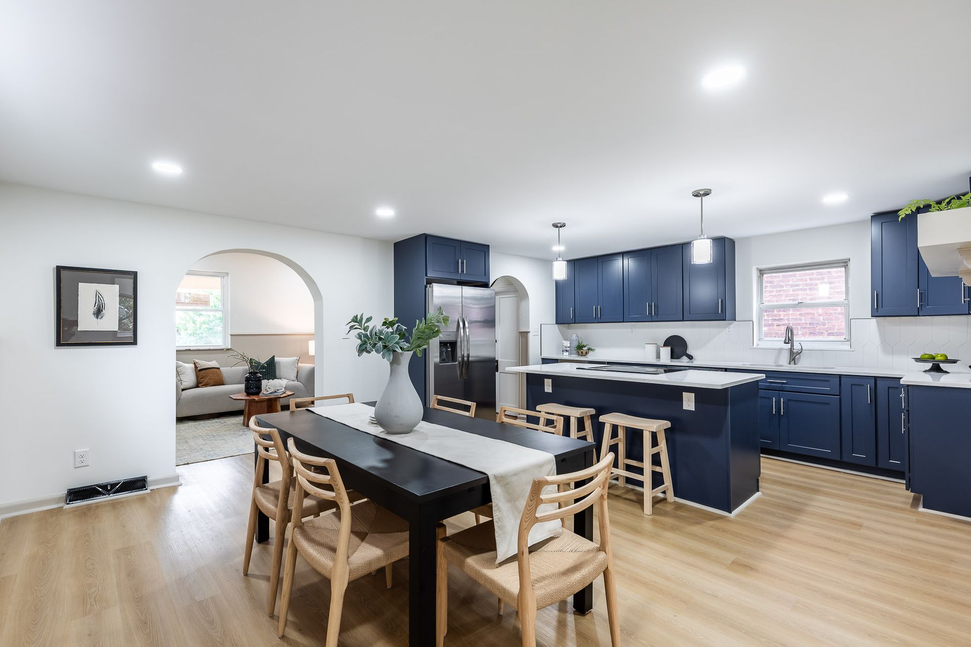 Open-concept kitchen and dining area with navy blue cabinets, a black dining table, and light wood flooring.