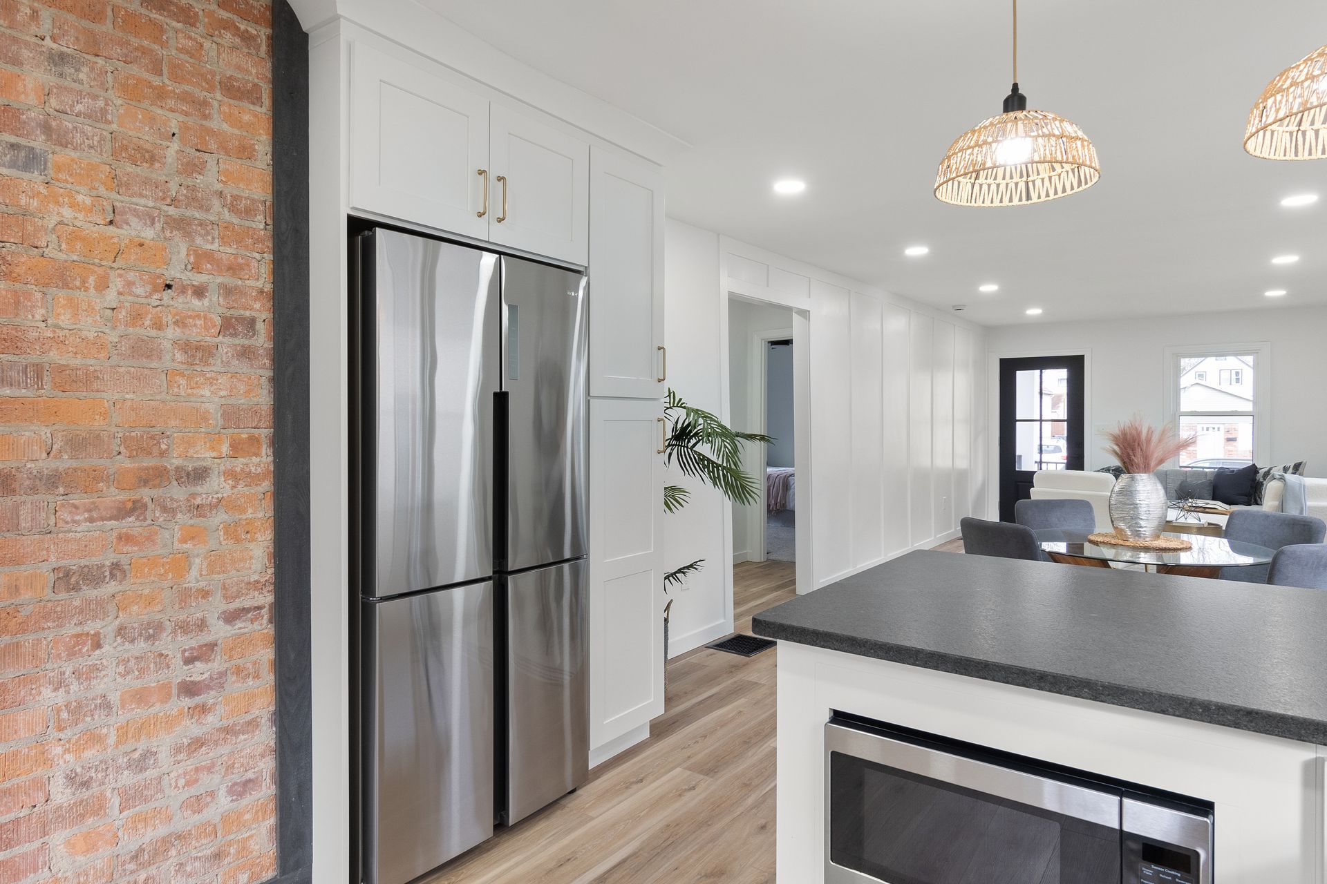 Modern kitchen with stainless steel refrigerator, brick wall, white cabinets, and island with a microwave.
