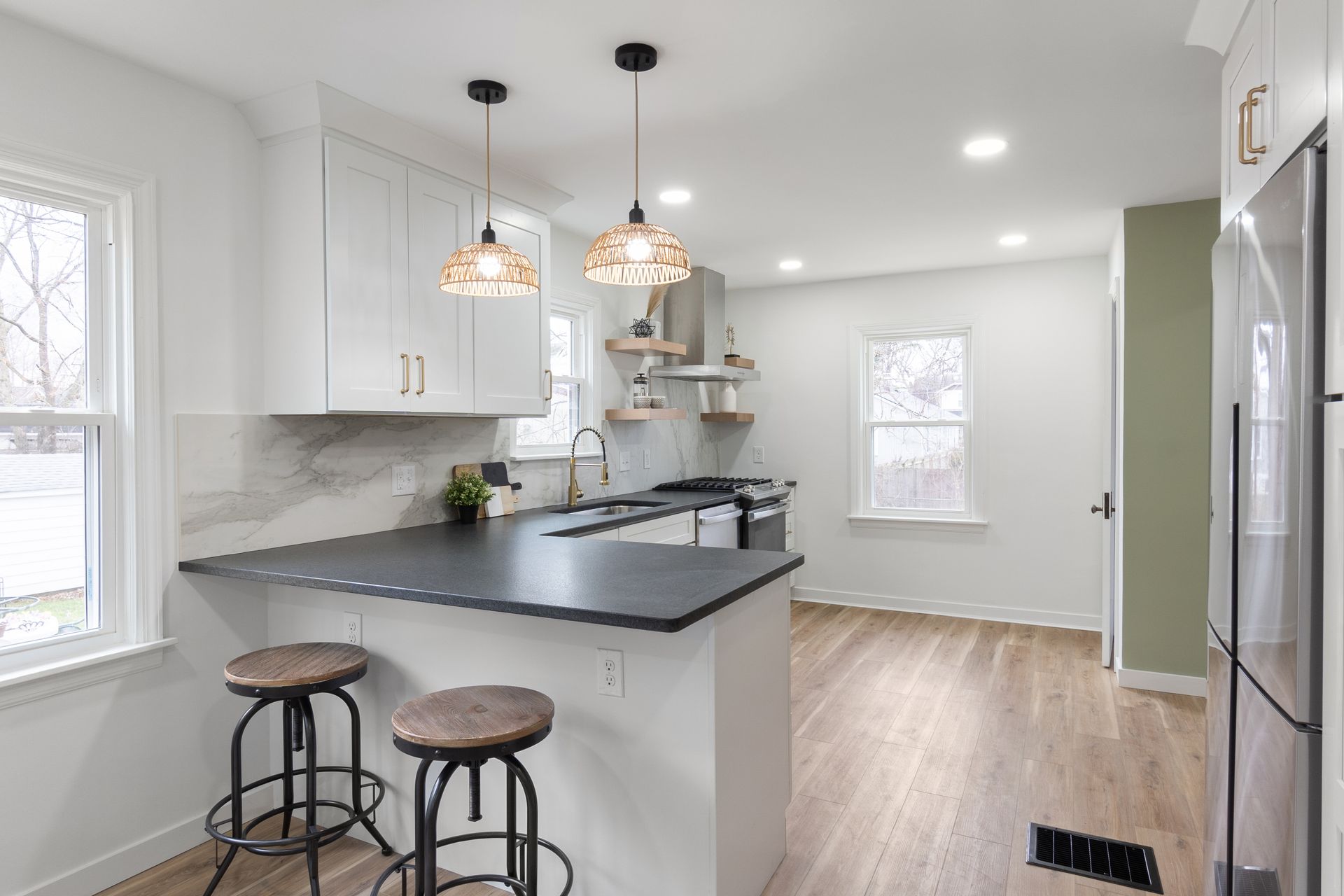 Modern kitchen with white cabinets, dark countertop, bar stools, and wicker pendant lights.