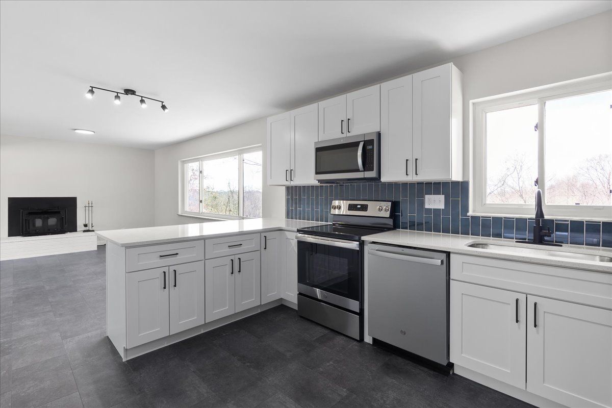 Modern white kitchen with stainless steel appliances, dark blue backsplash, and island.