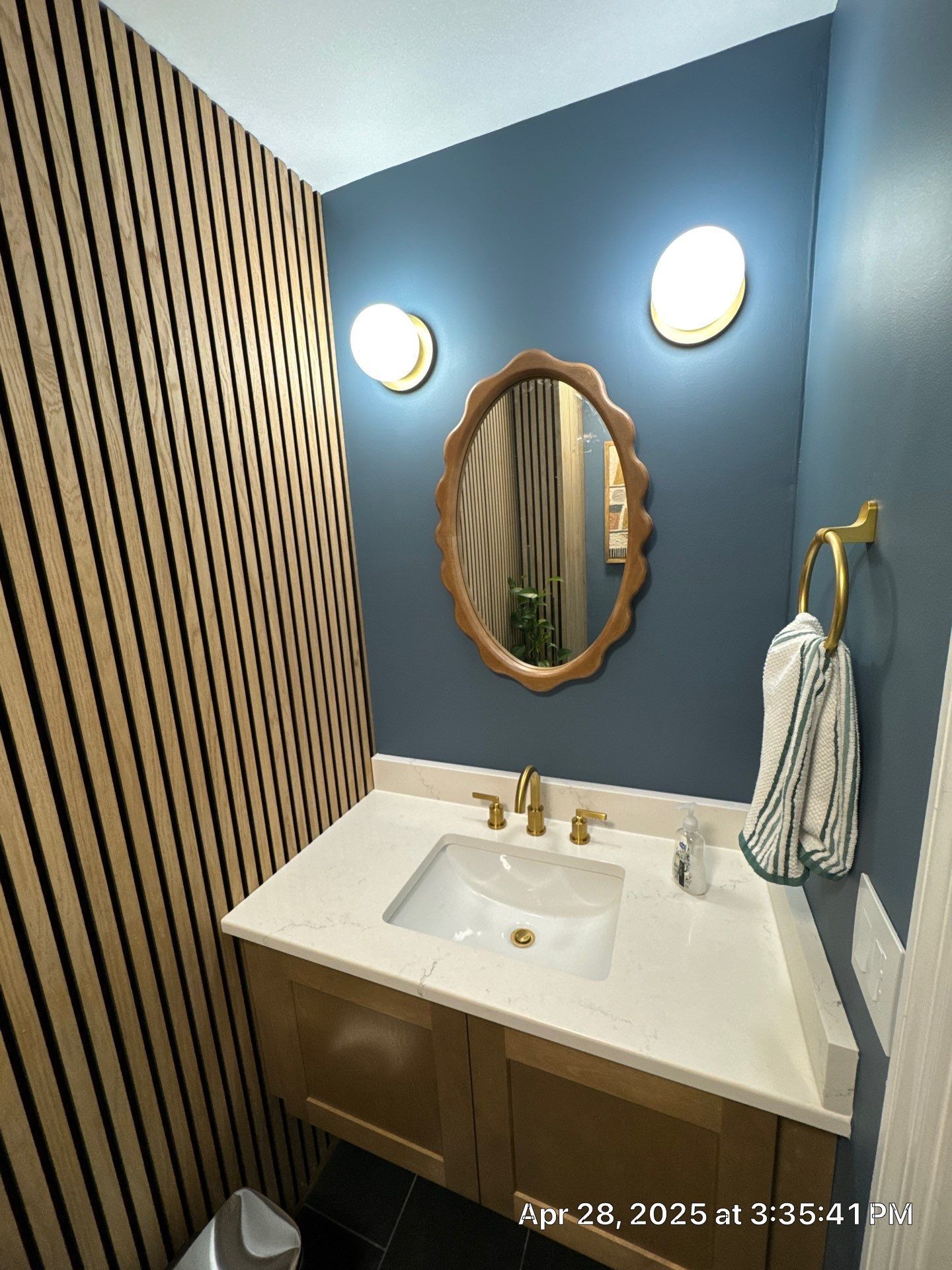 Small bathroom with a gold-framed mirror, blue wall, gold fixtures, and a wooden accent wall.