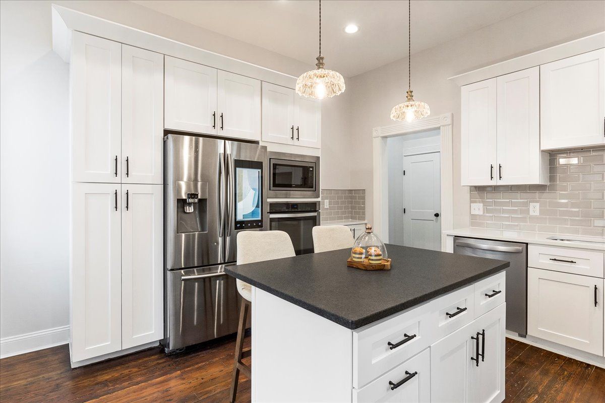 White kitchen with stainless steel appliances, dark island countertop, and wood floors.