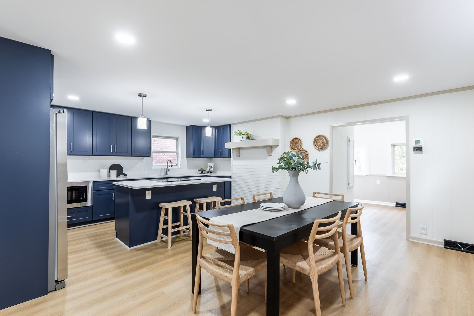 Modern kitchen with navy blue cabinets, an island, and a dining table with wooden chairs.