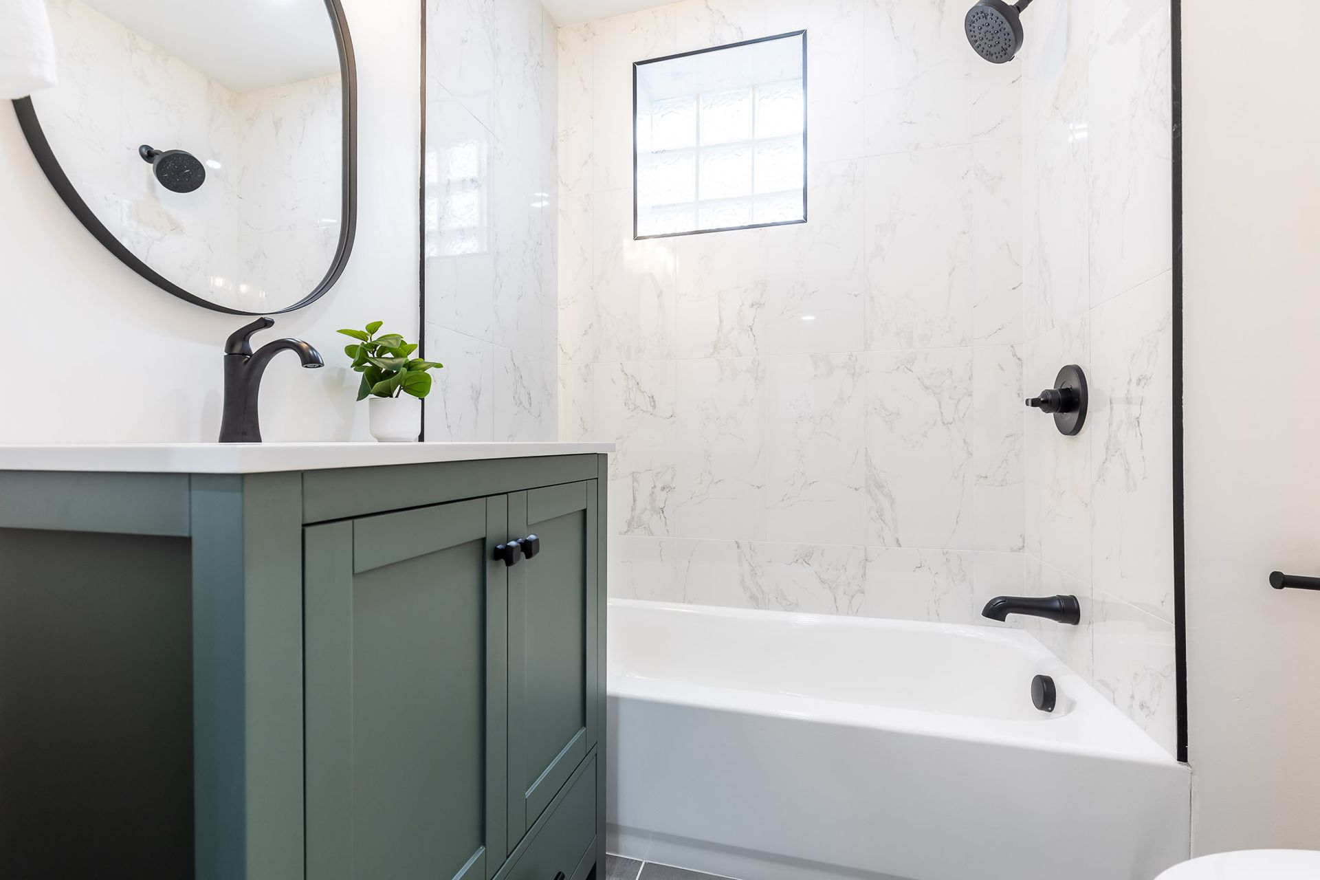 Bathroom with green vanity, white tub, black fixtures, and marble-look tile.