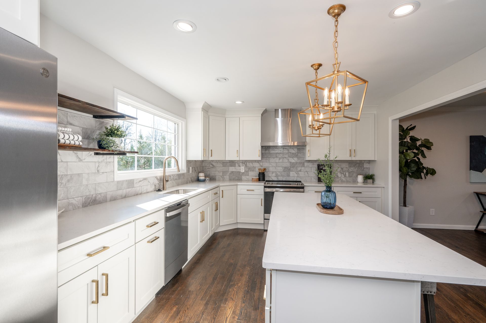Bright white kitchen with a large island, stainless steel appliances, and gold accents.
