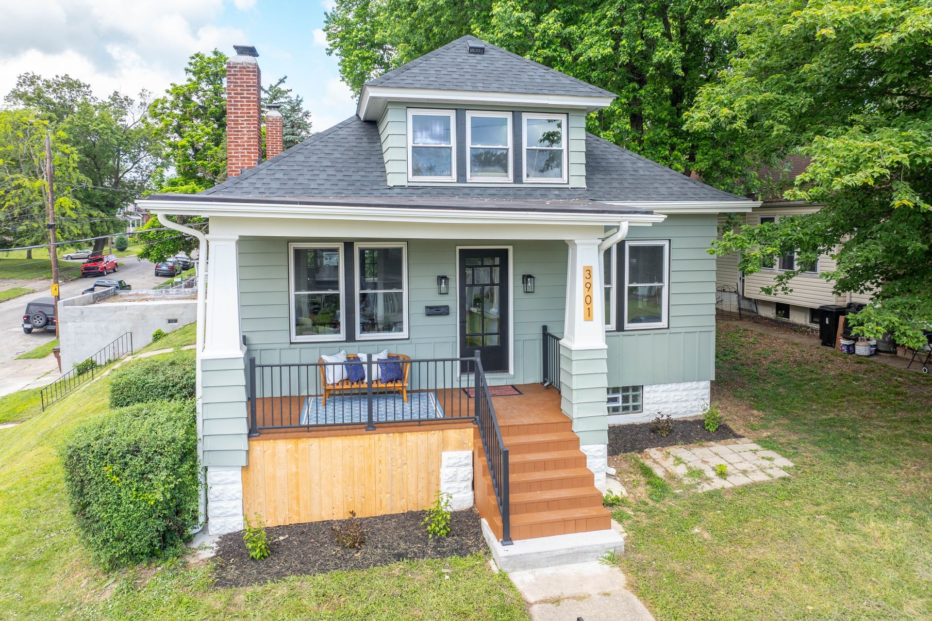 Green house with porch and wooden steps; trees and street in background.