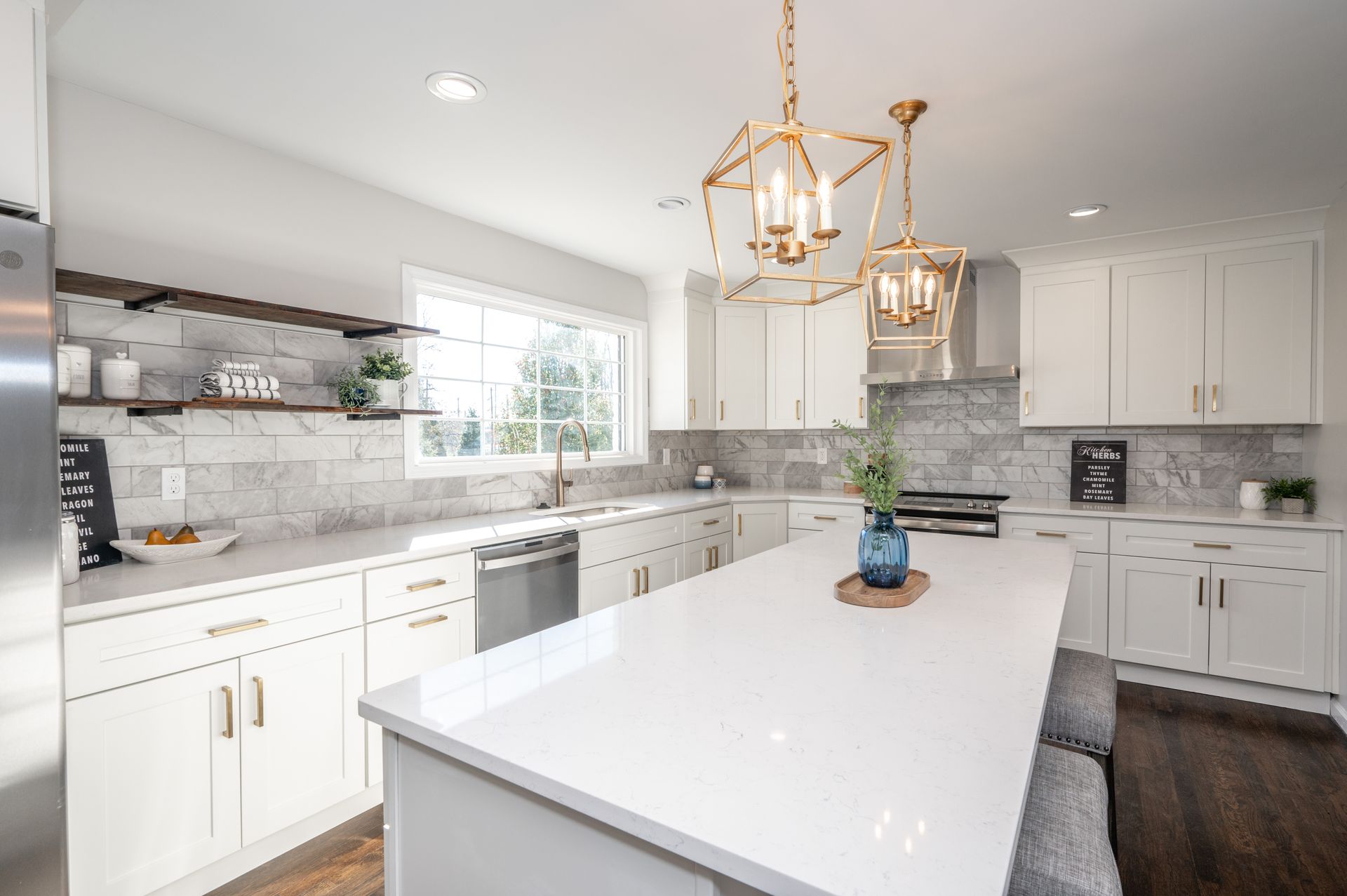 White kitchen with marble backsplash, stainless steel appliances, and gold light fixtures.