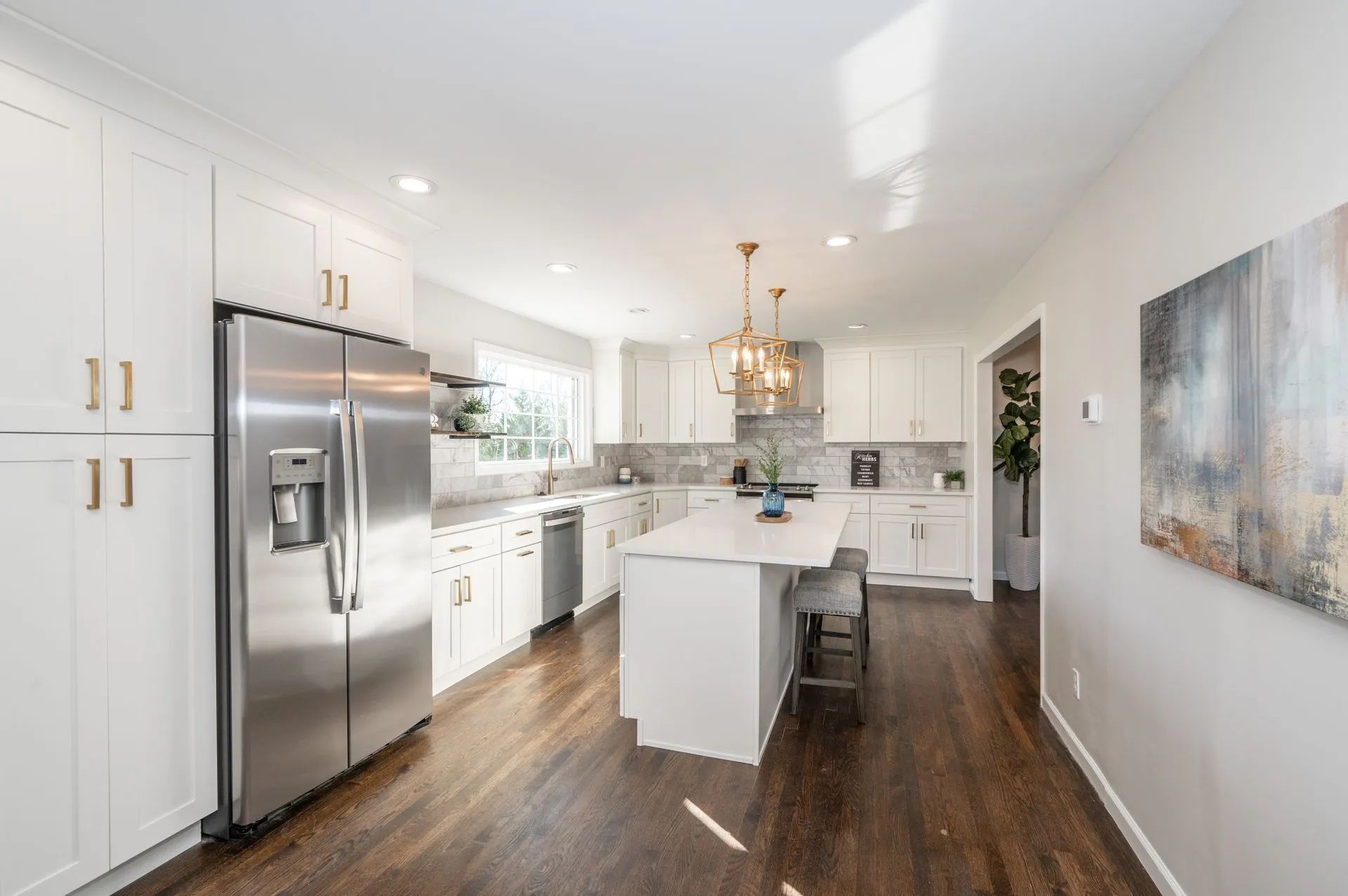 Modern white kitchen with stainless steel appliances, dark wood floors, and island.