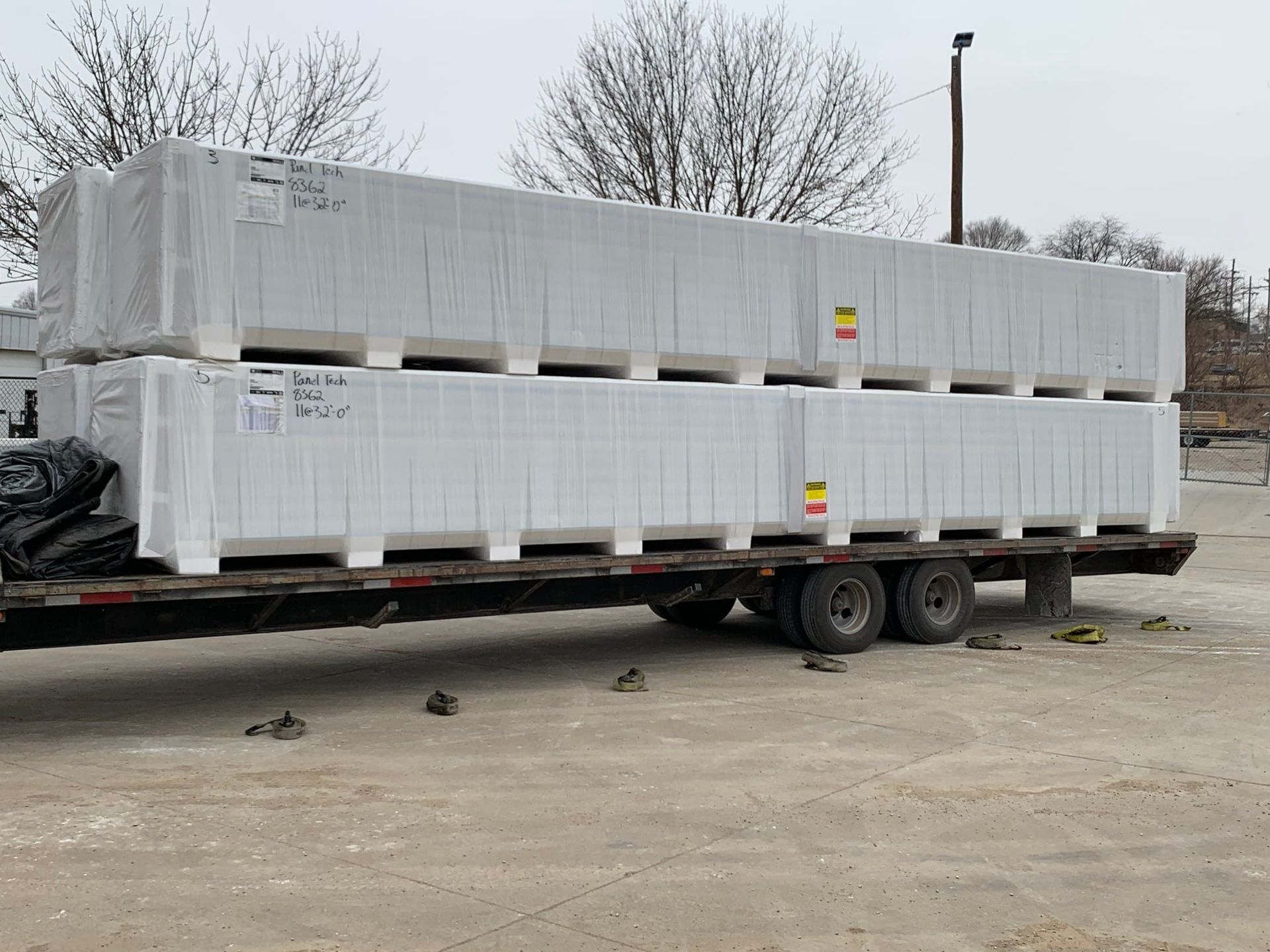 Two stacks of white-wrapped packages on a flatbed trailer, parked outdoors.
