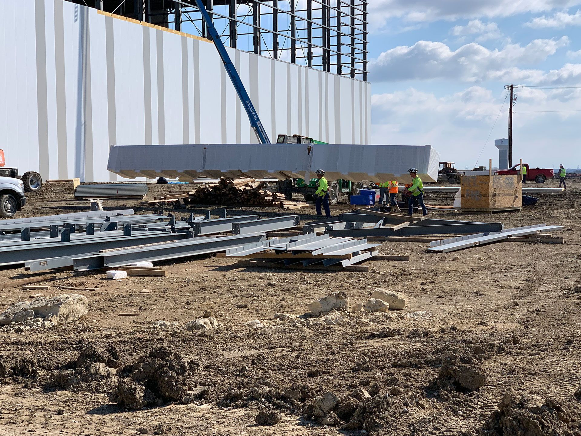 Construction site: A crane lifts a large concrete beam for building assembly, workers nearby.