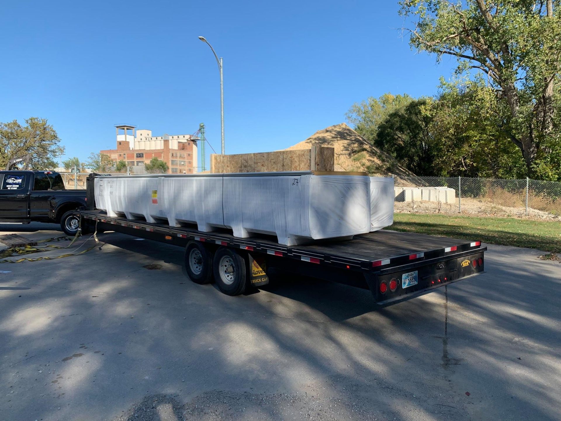 A large concrete barrier sits on a trailer pulled by a black truck on a road.