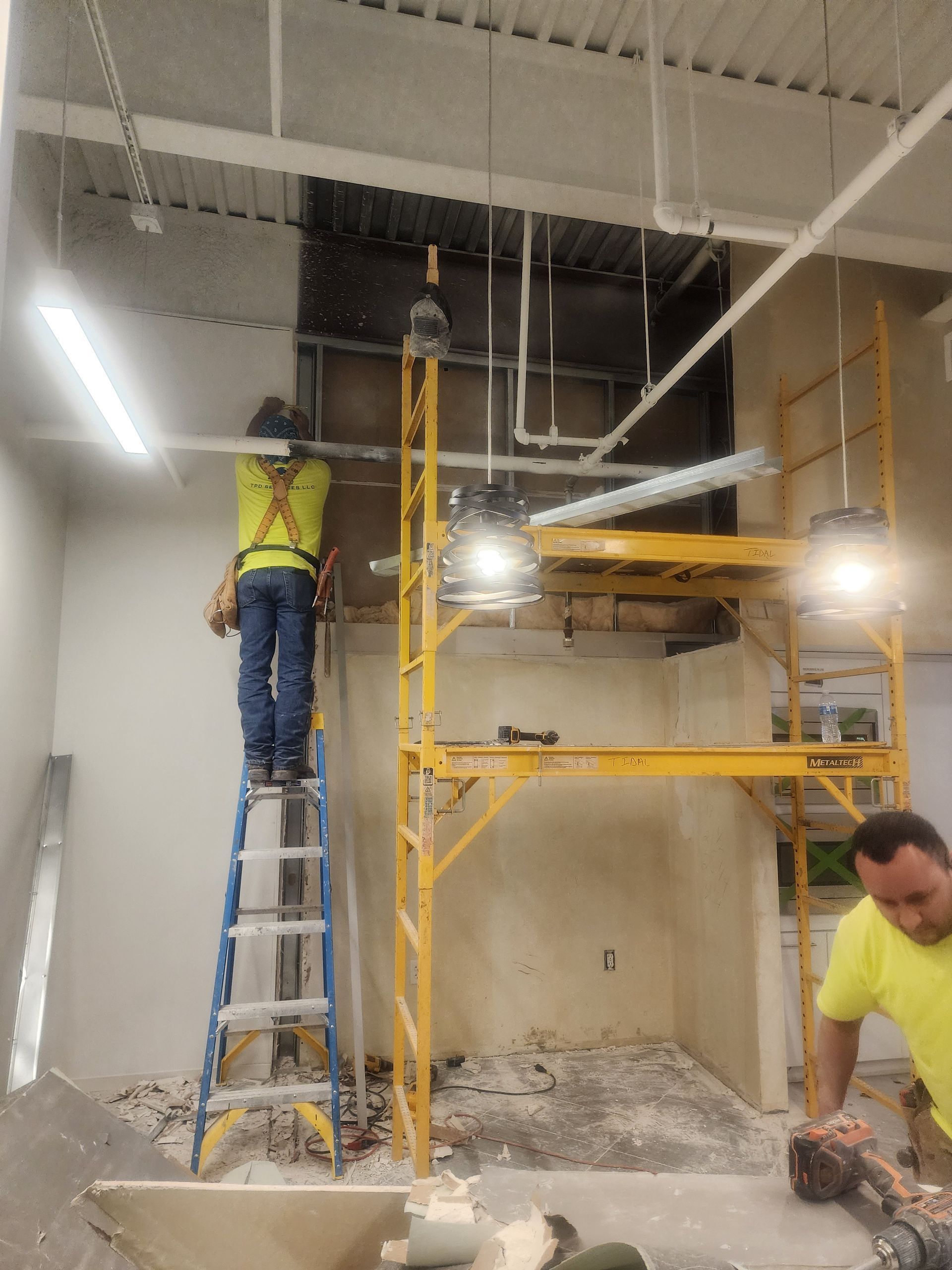 Construction workers on scaffolding repairing a damaged ceiling inside a building with exposed beams and debris.