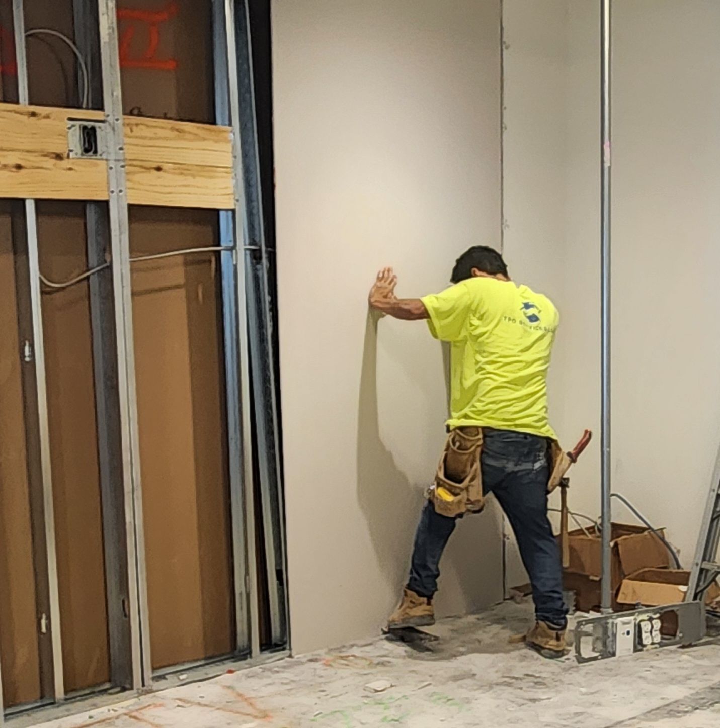 Worker in a neon yellow shirt installing drywall in an unfinished room.