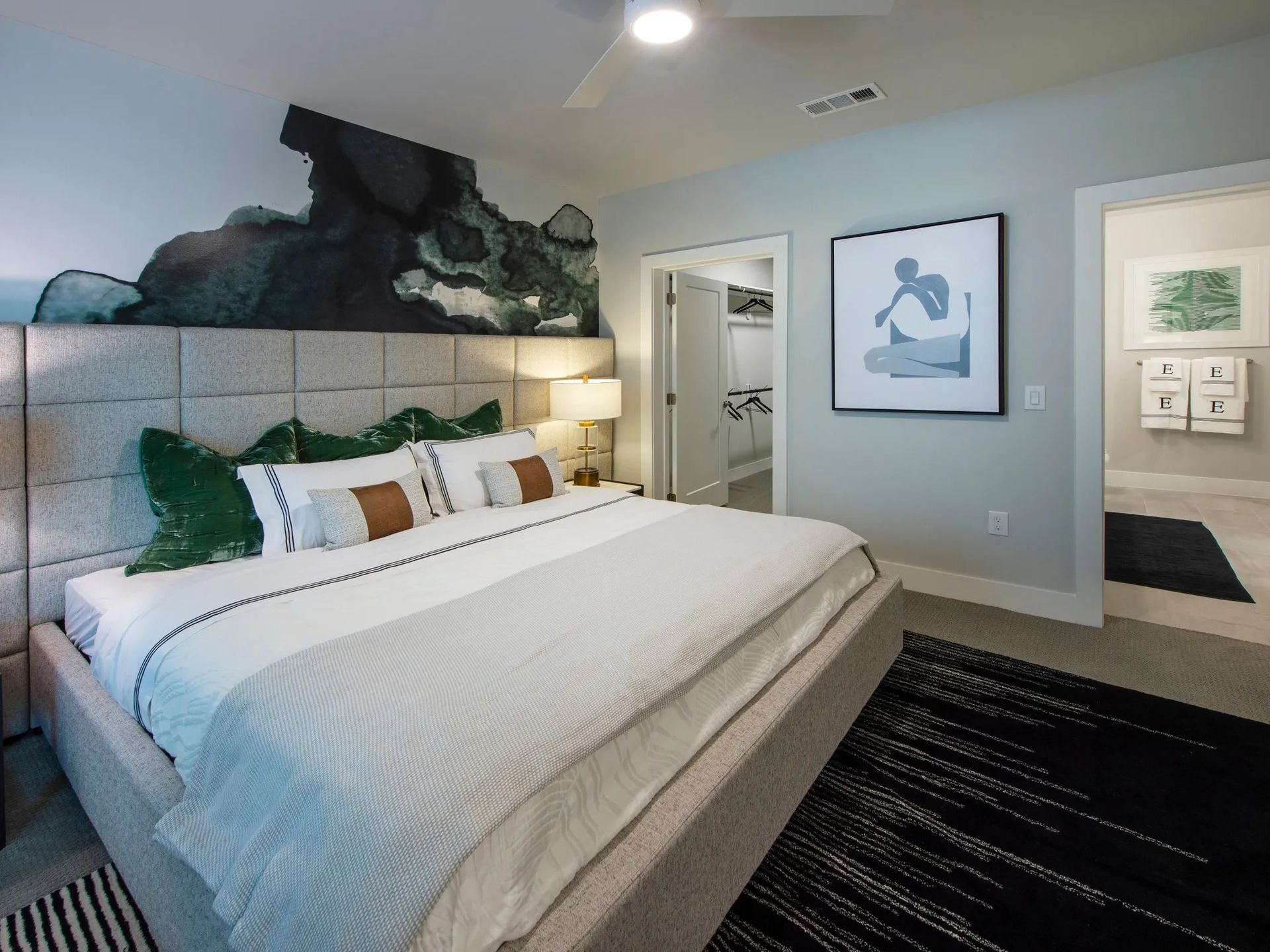 Modern bedroom with a white bed, green pillows, dark rug, and framed wall art