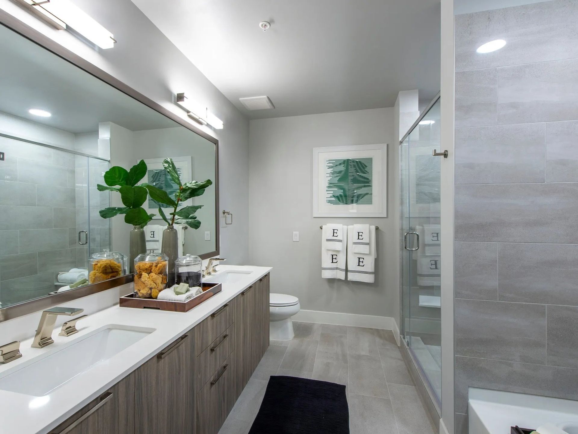 Modern bathroom with double sink vanity, glass shower, and gray tile walls
