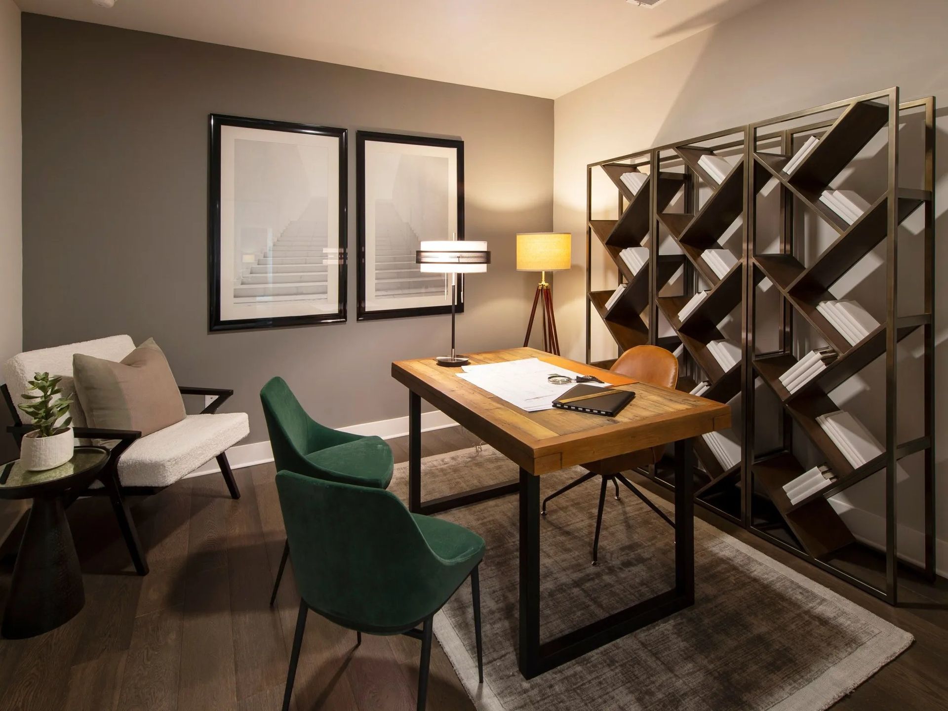 Cozy home office with desk, green chair, lamp, wall art, and tall shelving unit