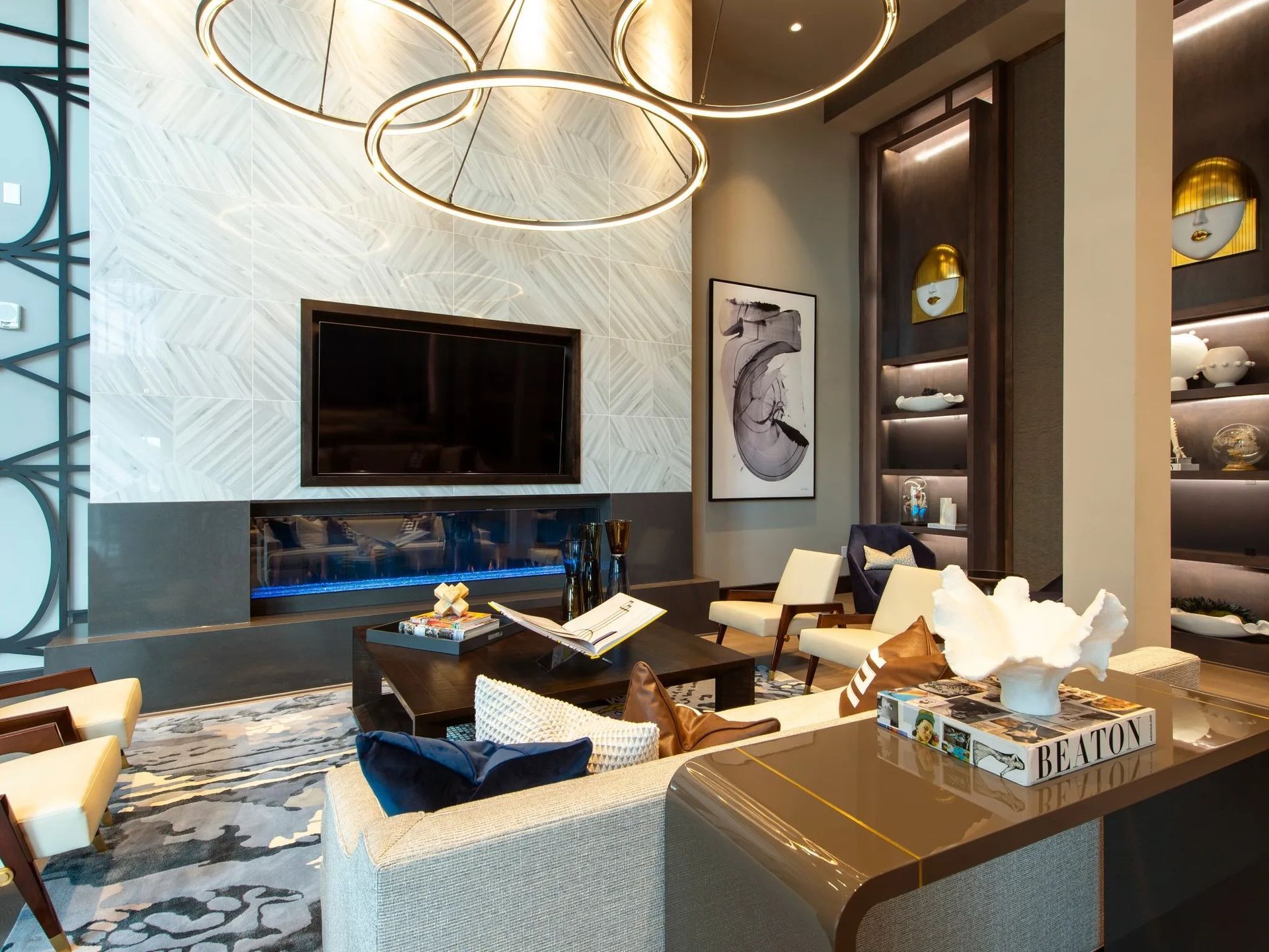 Modern living room with a wall-mounted TV, circular chandeliers, and neutral seating by a fireplace