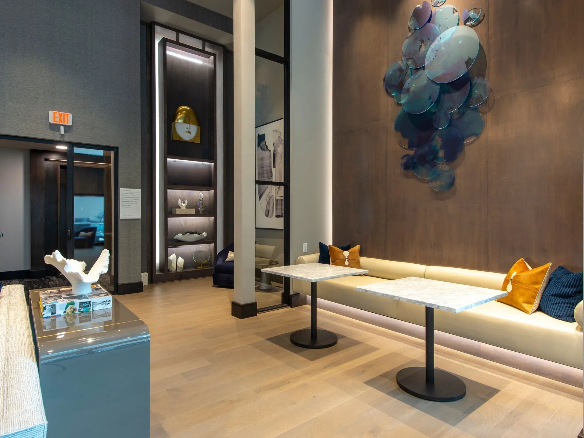 Modern lounge with white benches, small tables, blue accents, and abstract wall art.