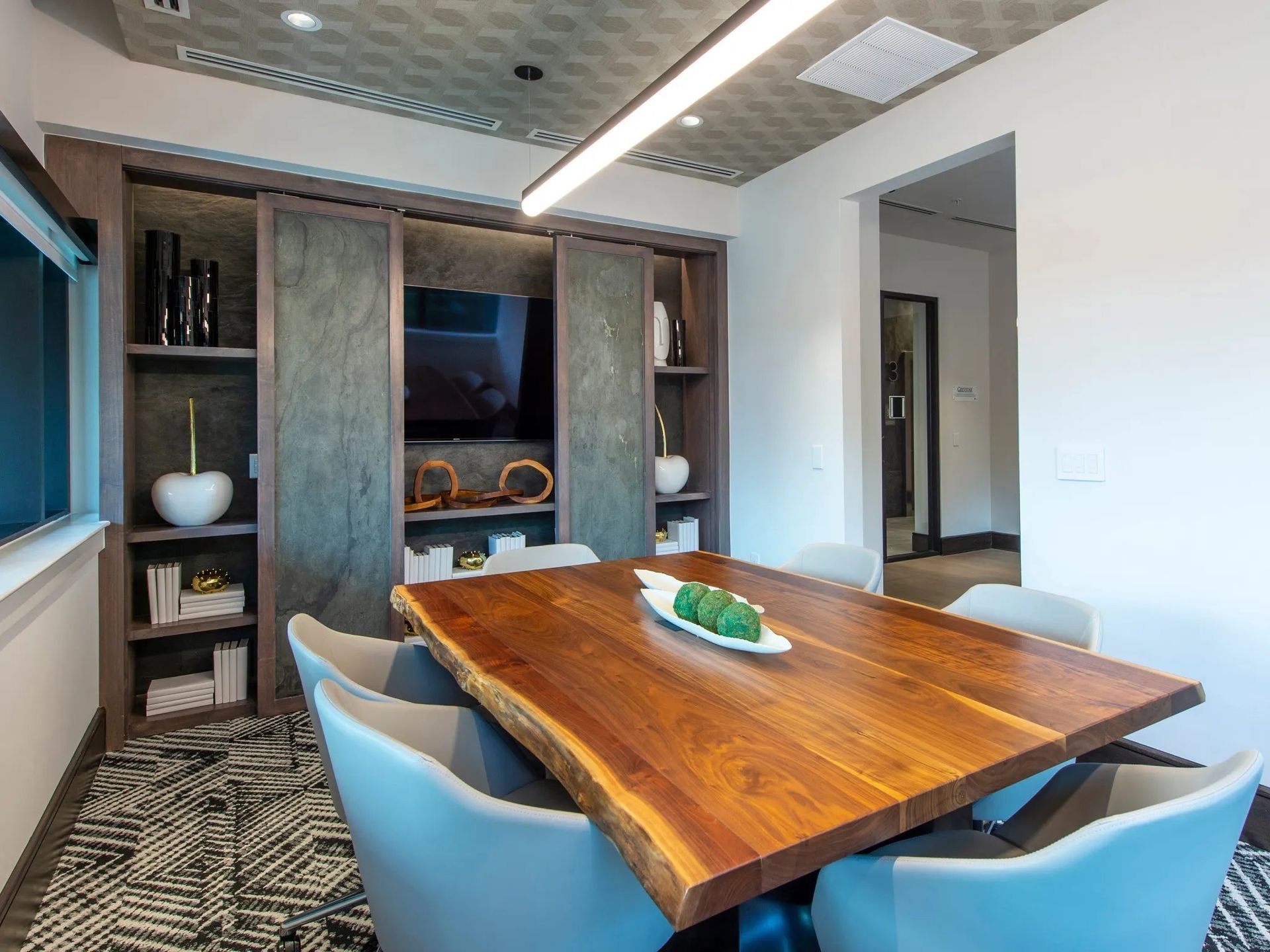Modern dining room with a wooden table, blue chairs, and built-in shelving around a TV