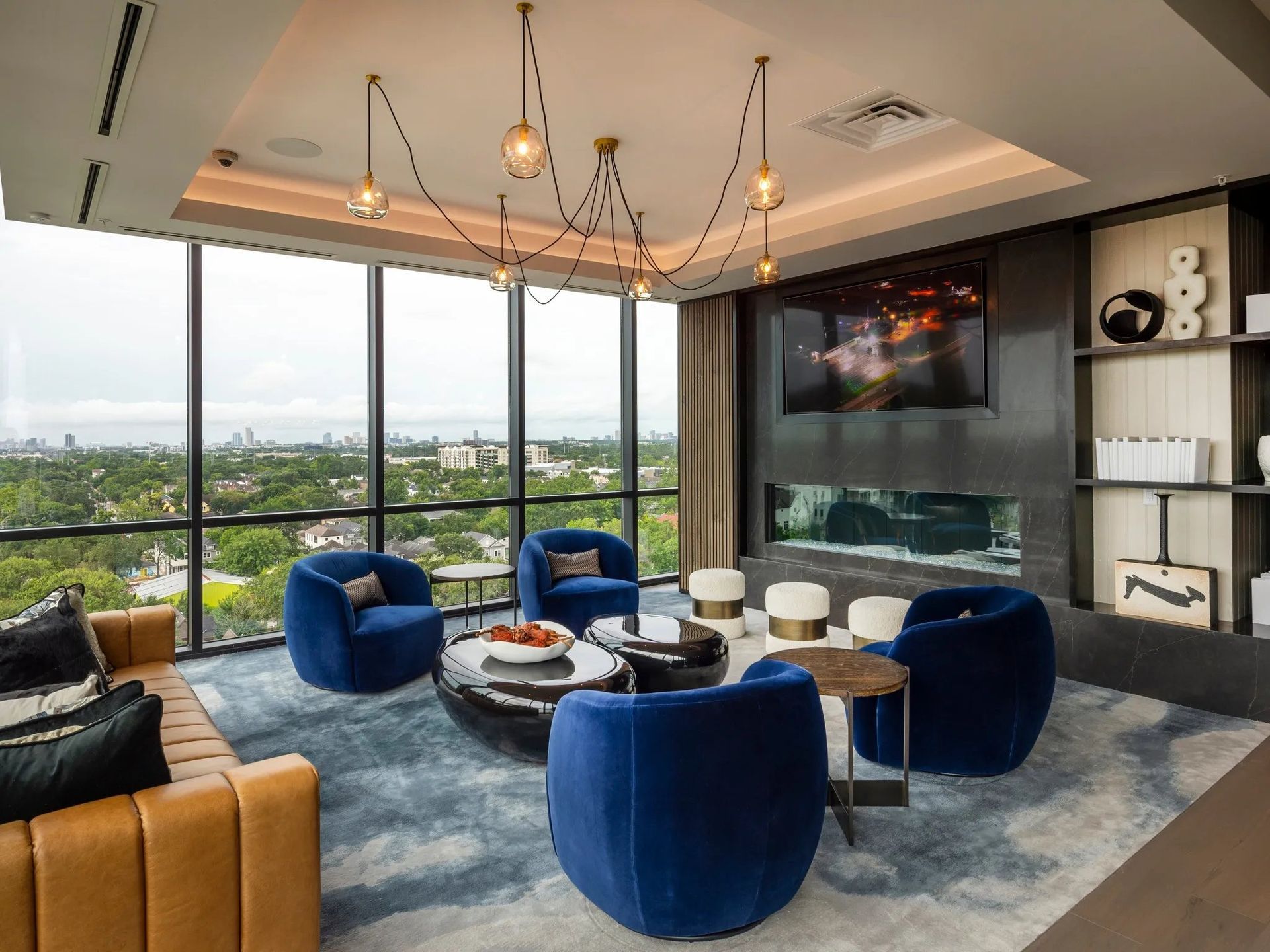 Modern lounge with blue velvet chairs, round tables, fireplace, and city-view windows