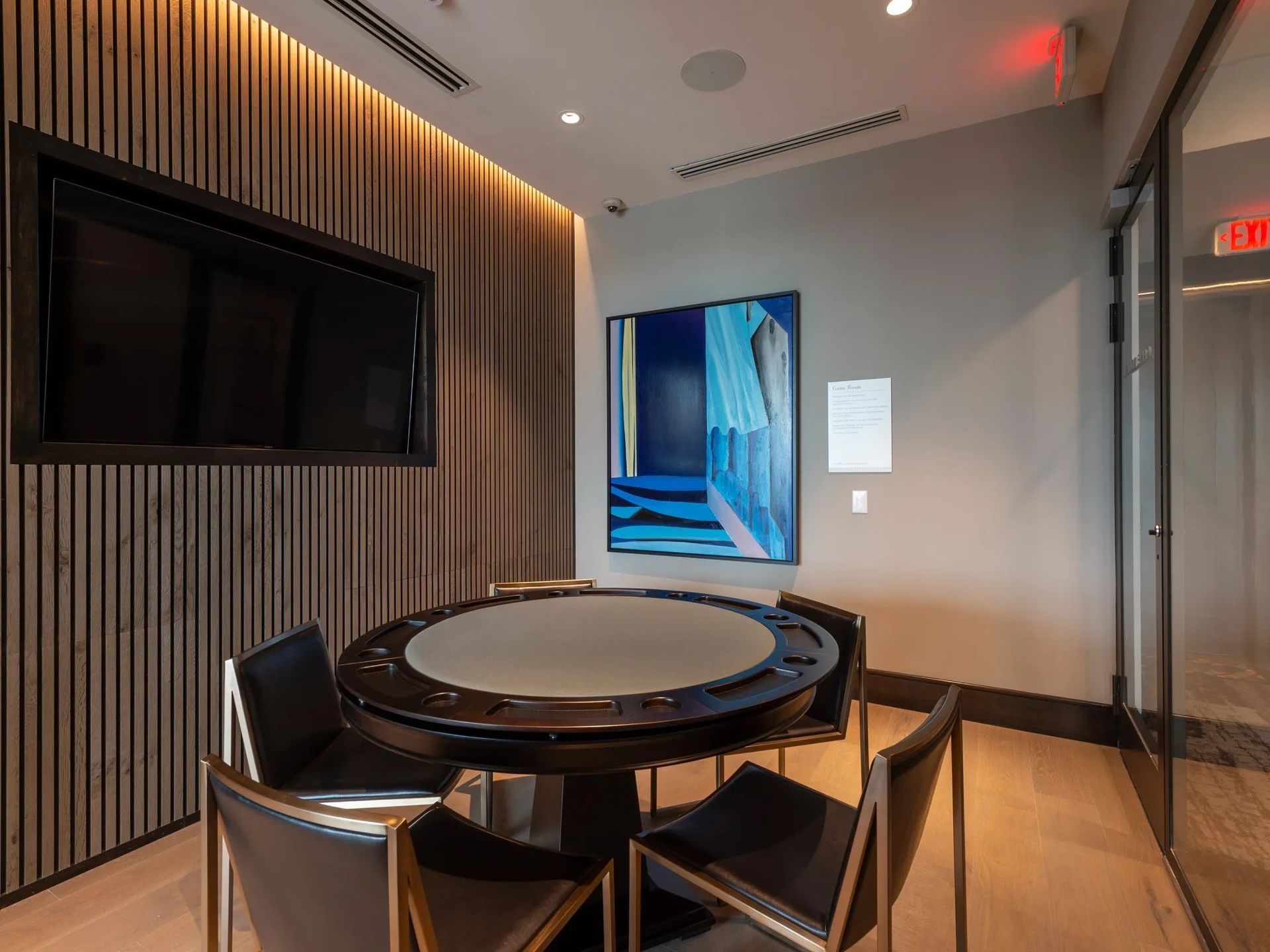 Modern lounge with a round table, black chairs, wall-mounted TV, and blue artwork on the wall.
