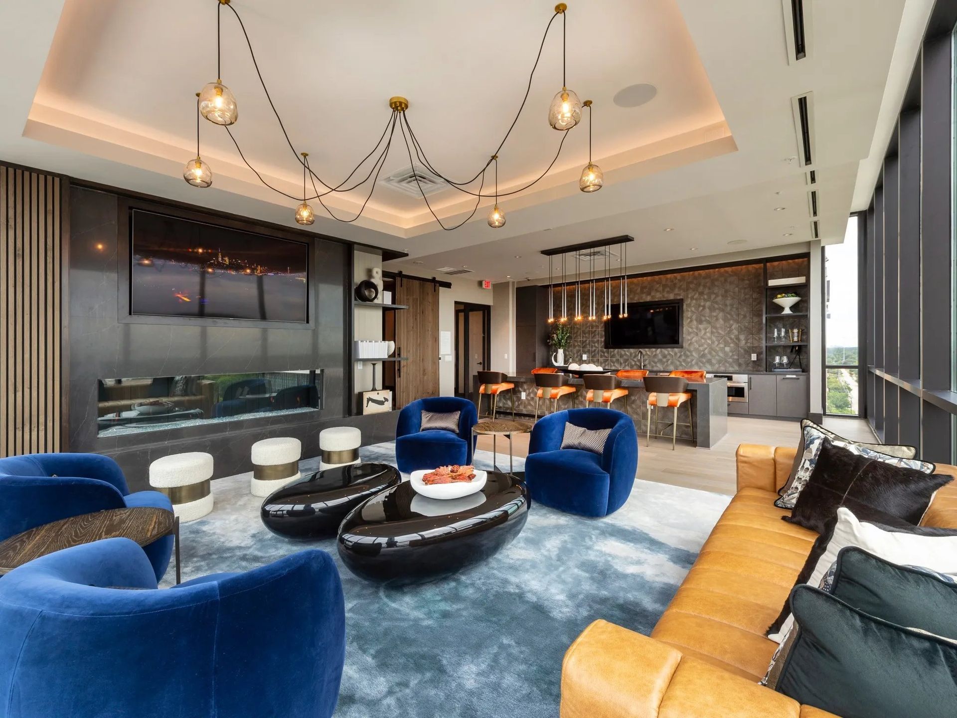 Modern living room with blue velvet chairs, gold chandelier, and open kitchen in the background