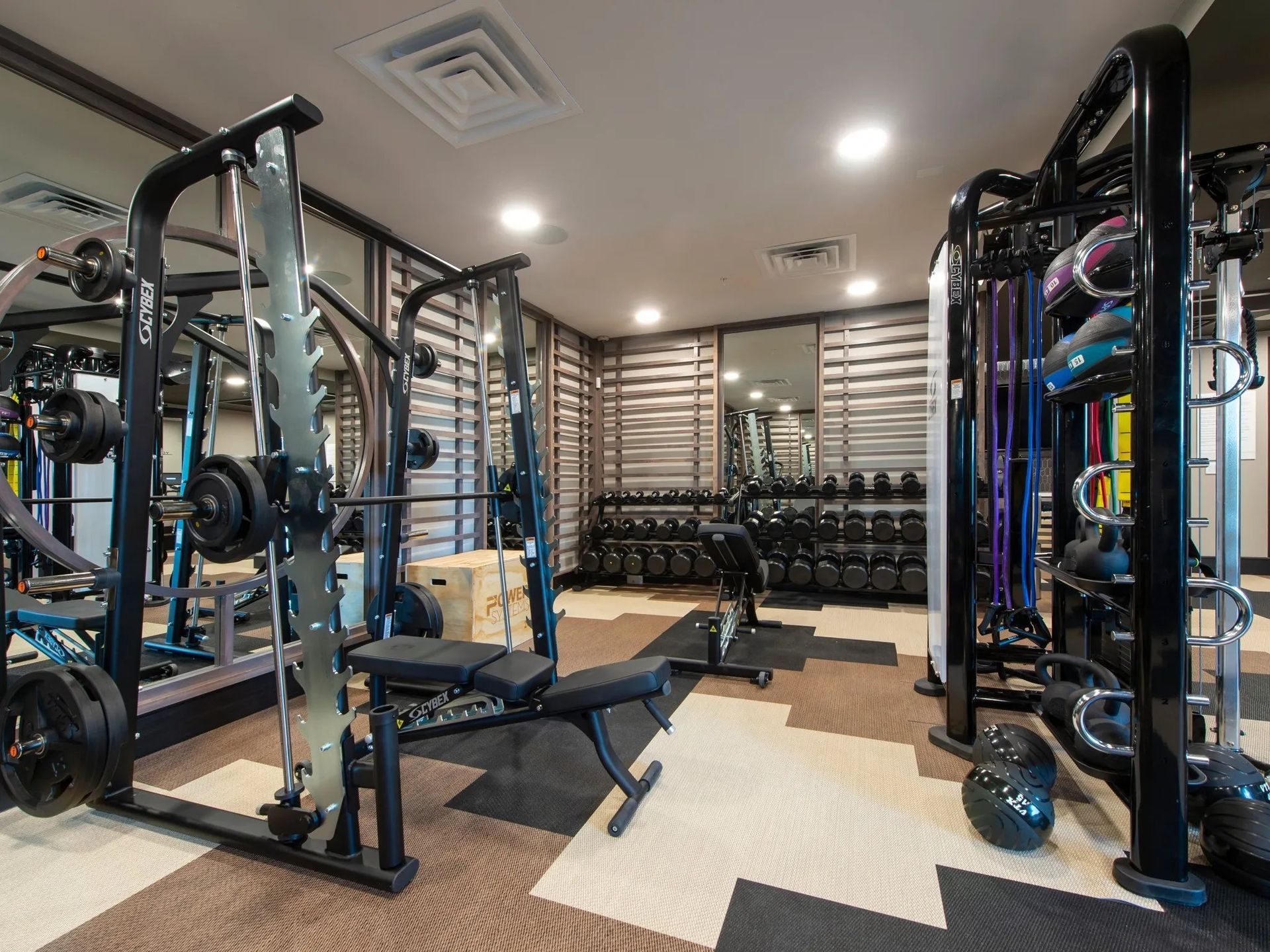 Modern gym with cable machines, dumbbells, and a bench on a light wood floor