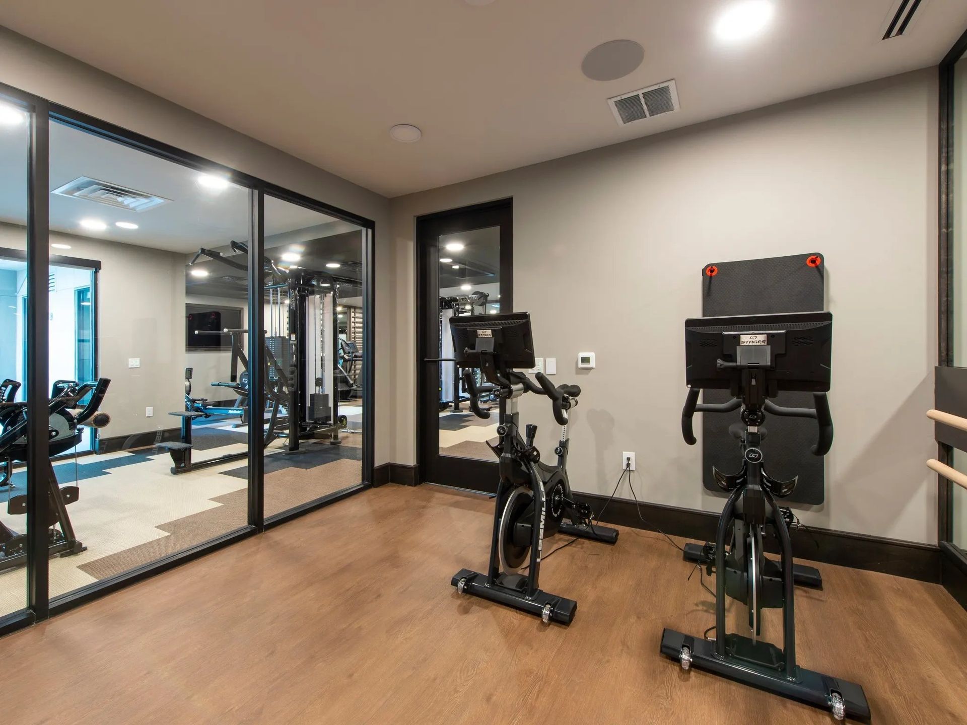 Indoor gym room with two stationary bikes on wood floors beside glass-walled workout area