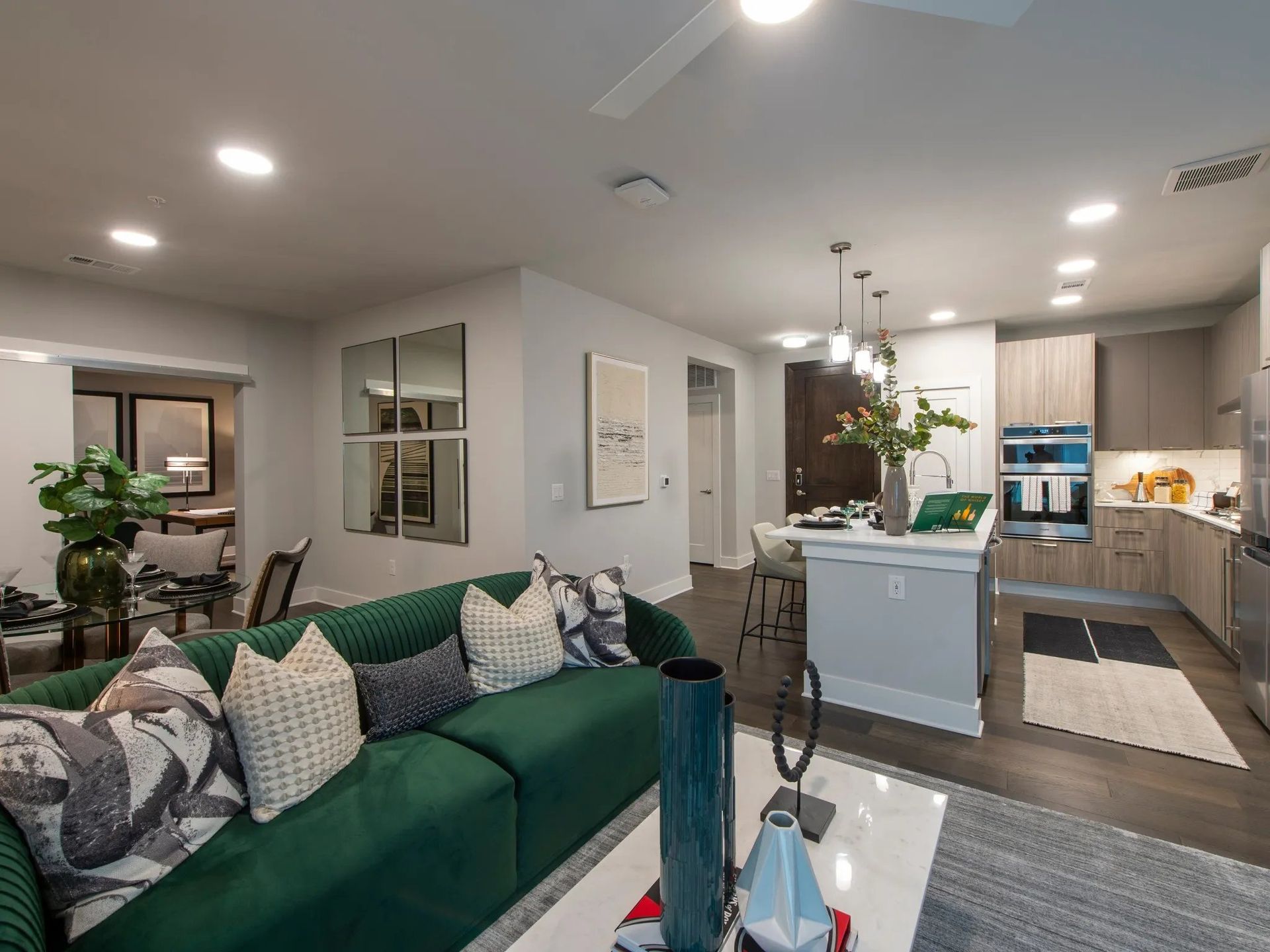Open-concept living room with green sofa, dining table, and kitchen island under pendant lights