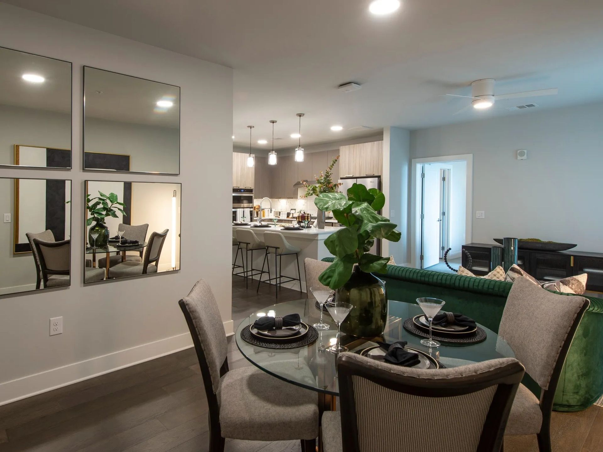 Modern open-concept dining area with glass table, chairs, wall mirrors, and a view into a bright kitchen