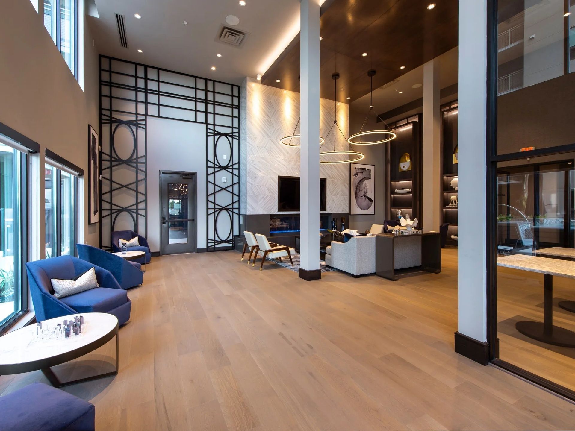 Modern hotel lobby with high ceilings, blue chairs, lounge seating, and warm wood floors
