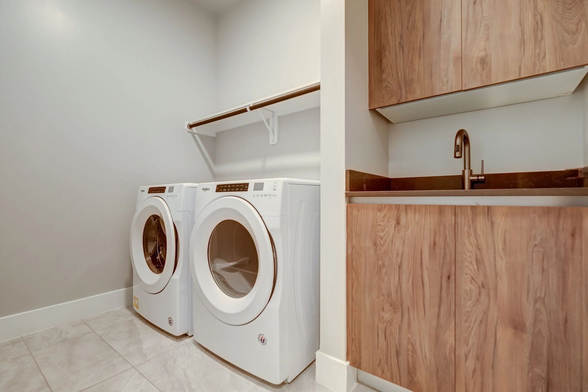 Laundry room with white washer and dryer beside a small wood vanity and sink
