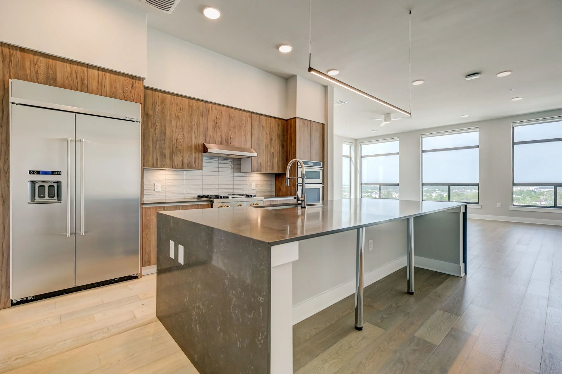 Modern kitchen with stainless steel appliances, large island, light wood floors, and bright windows