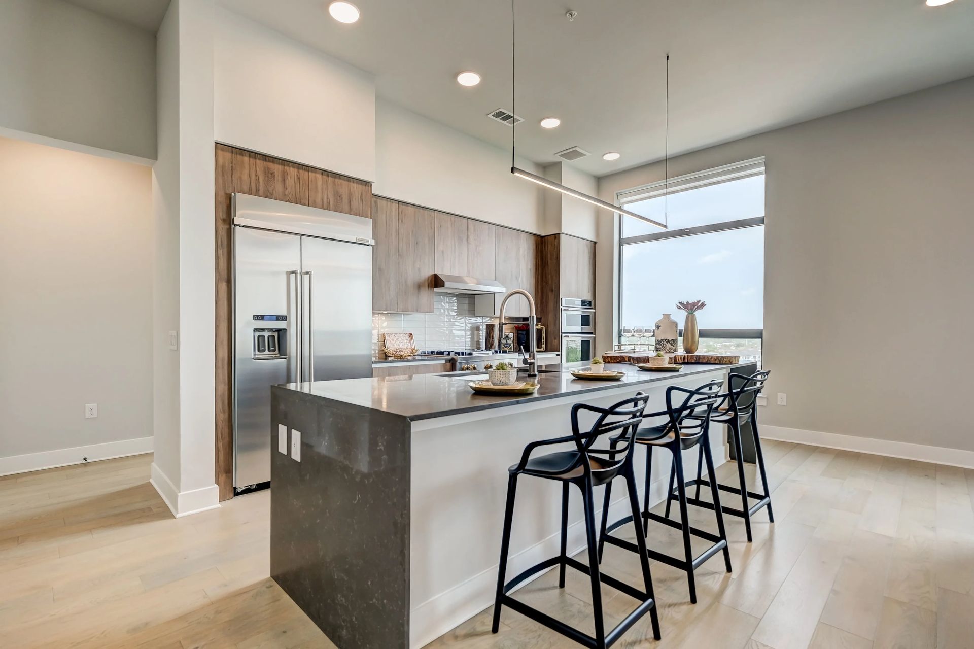 Modern open kitchen with island, black barstools, stainless appliances, and large windows