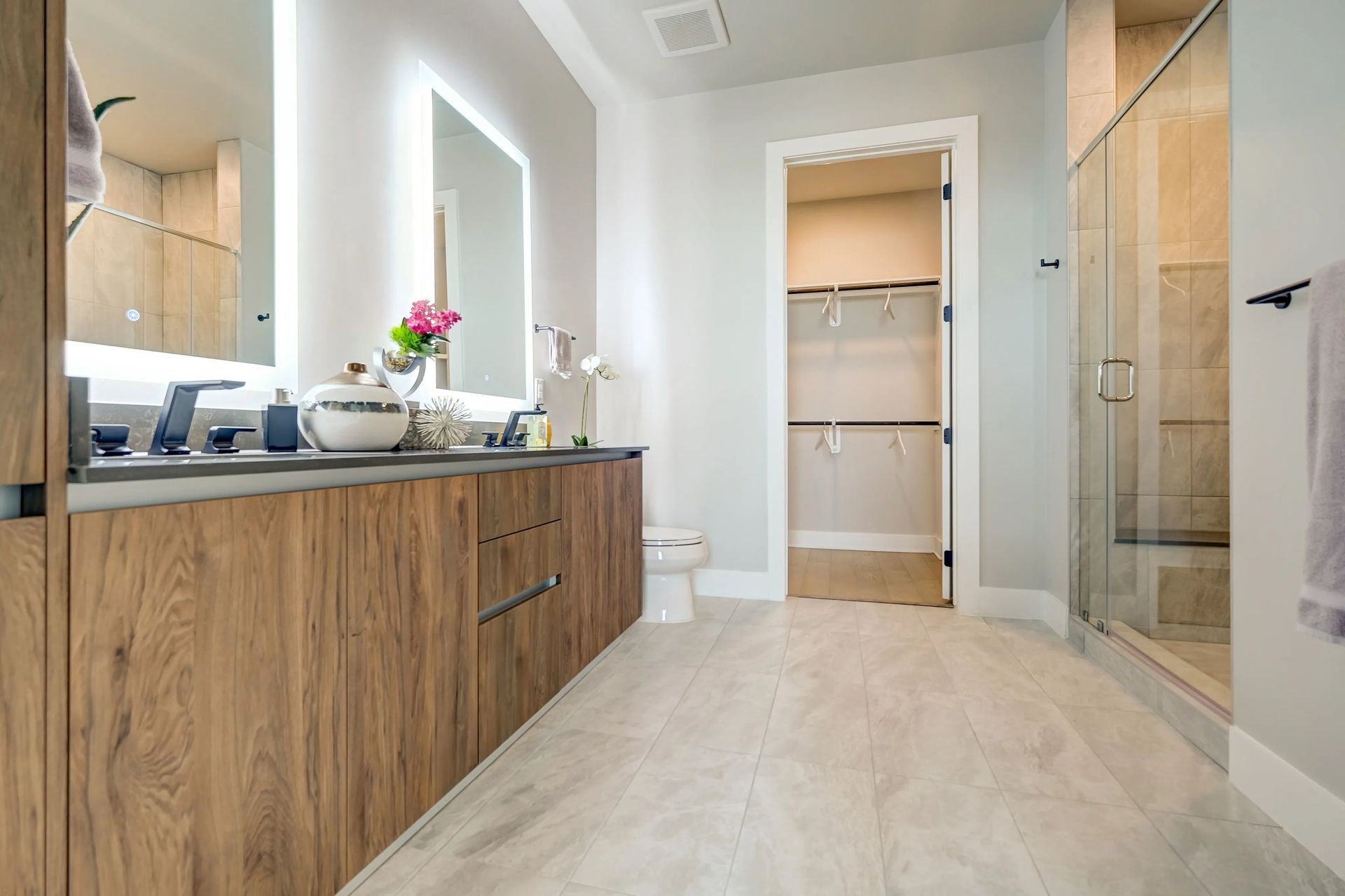 Modern bathroom with double wood vanity, large mirror, walk-in shower, and tiled floor