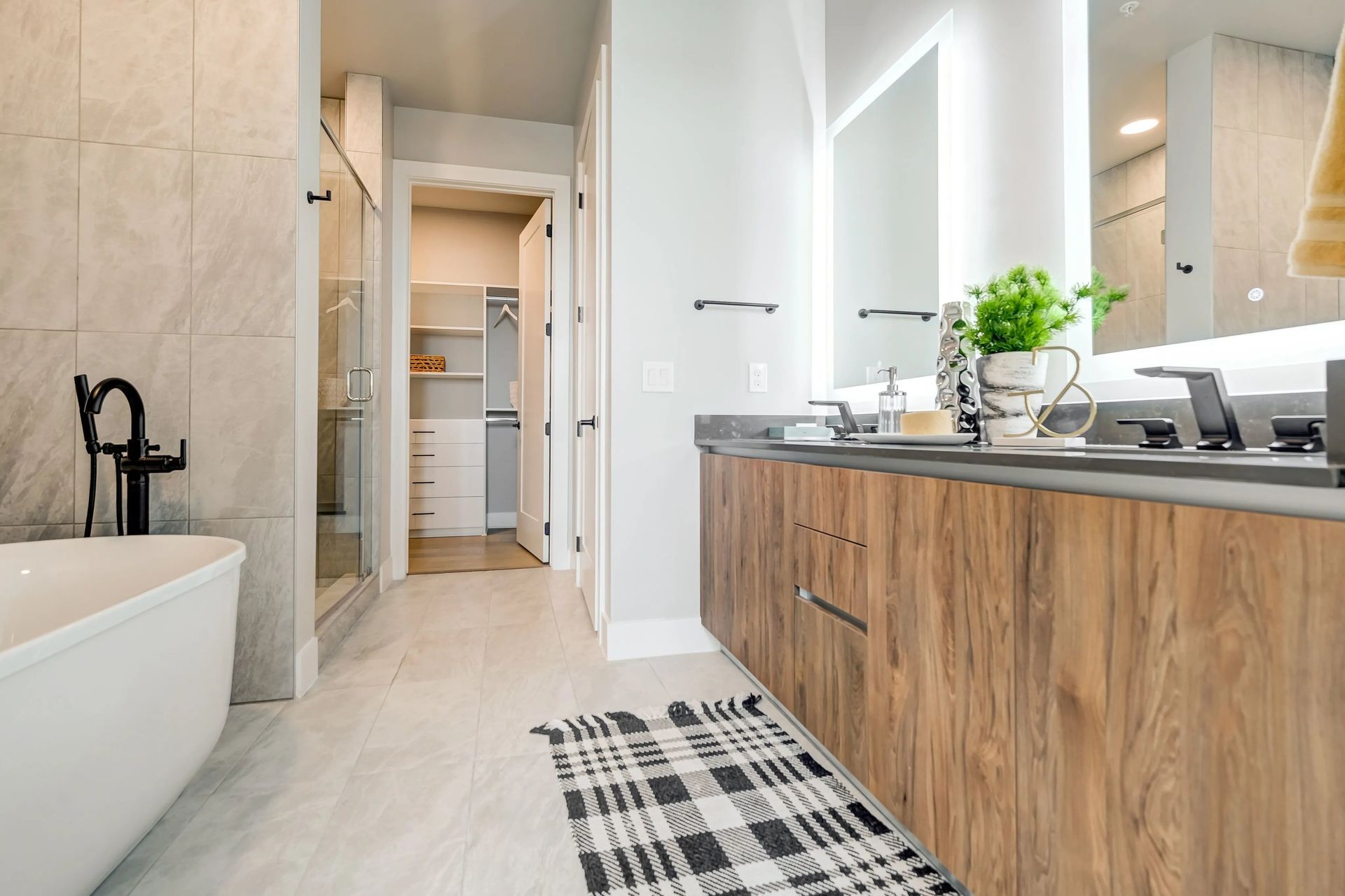 Bright modern bathroom with freestanding tub, wood vanity, and black-and-white rug.