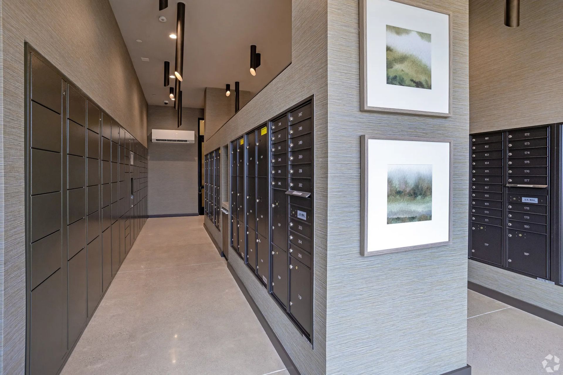 Apartment mailroom with black mailboxes along a beige hallway and framed wall art