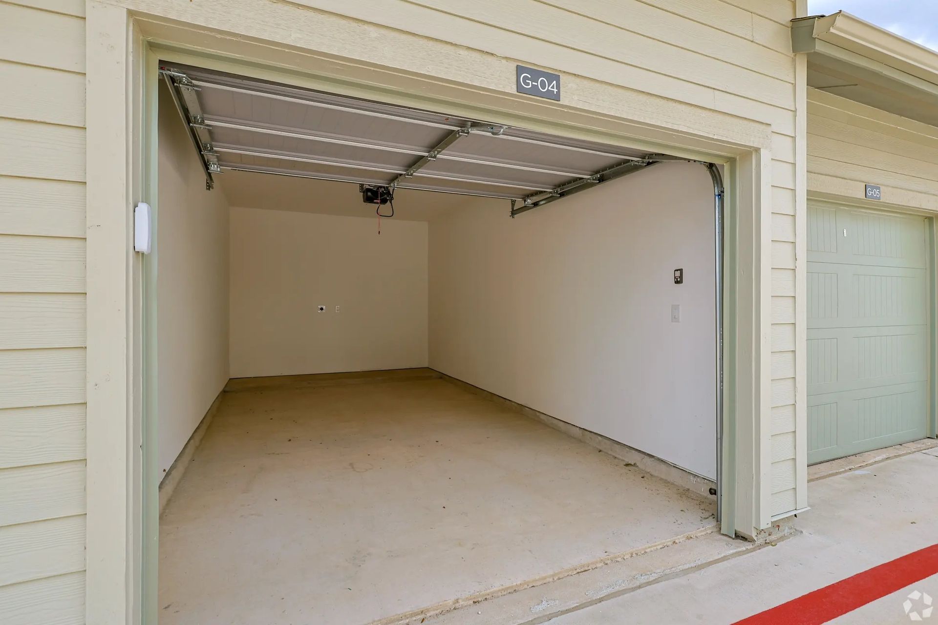 Empty beige garage with open overhead door and light-colored concrete floor