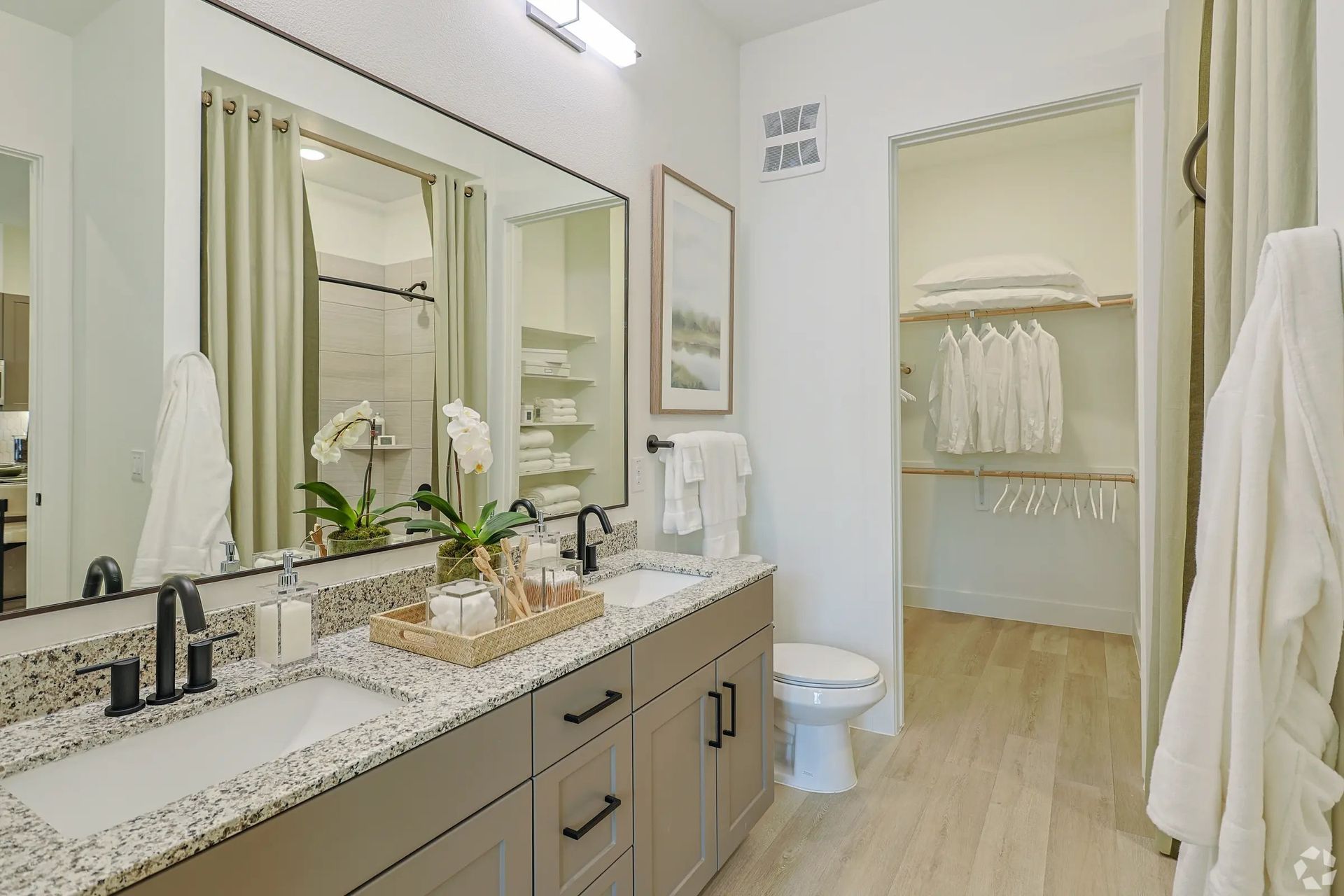 Bright bathroom with double vanity, large mirror, and open closet in soft beige tones